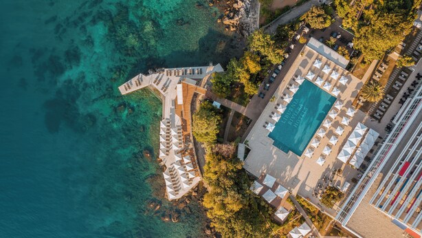 Vista aérea de un resort con piscina, varios sombrillas de playa y un muelle que se adentra en el agua.