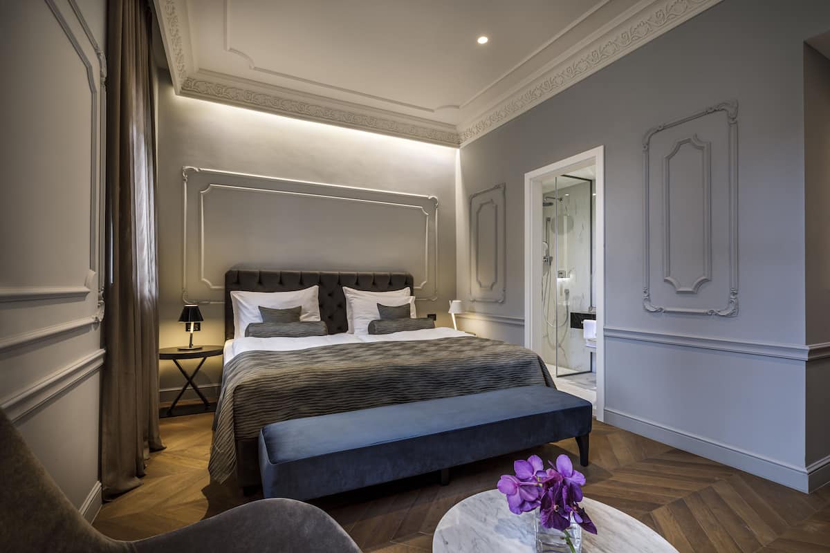 A modern bedroom with a large bed, bedside tables, a bench, and a mirror.