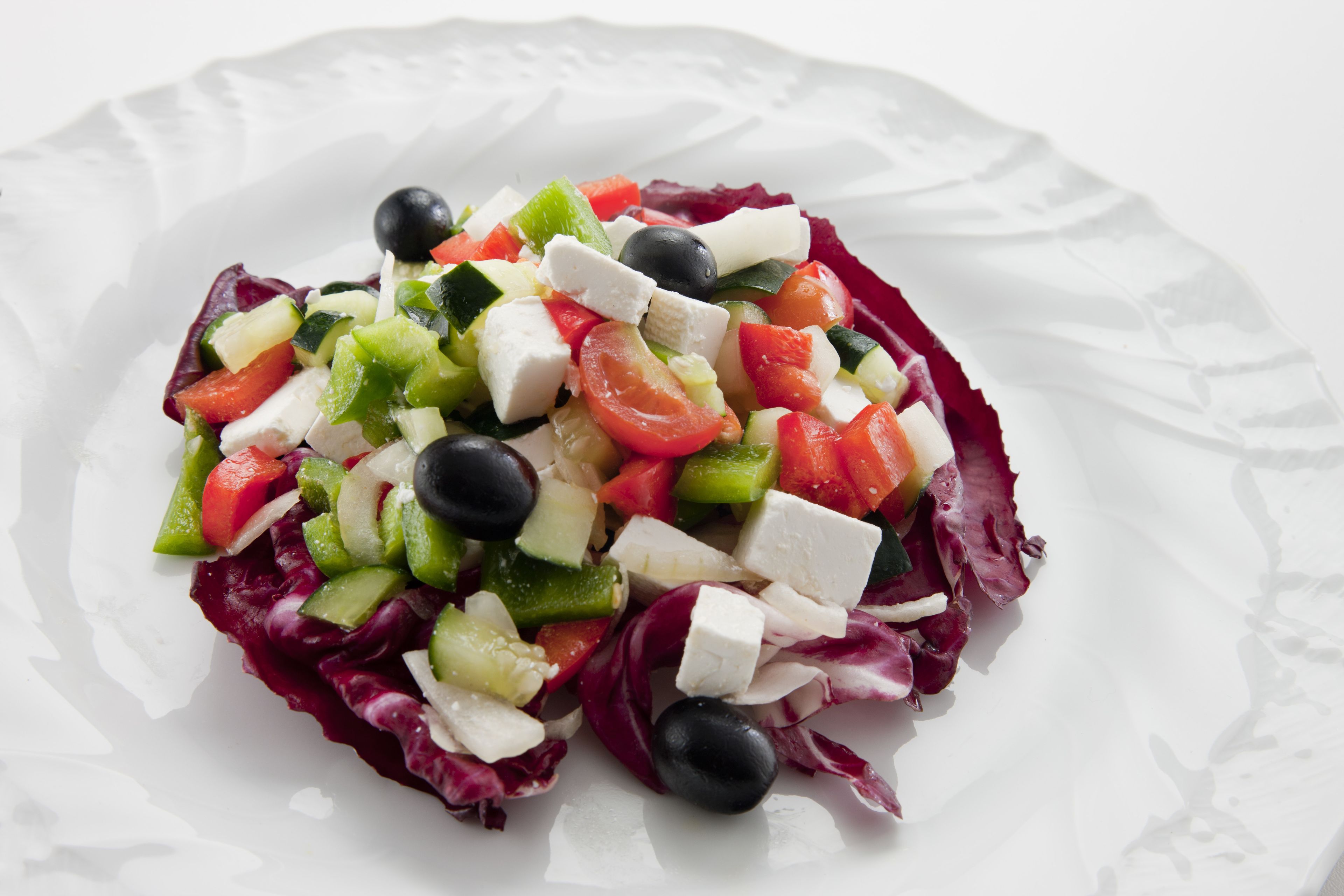 A white plate with a salad consisting of tomatoes, cucumbers, olives, and cheese.
