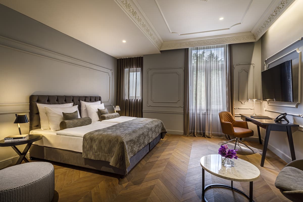 A modern hotel room with a large bed, a desk, a chair, and a TV.