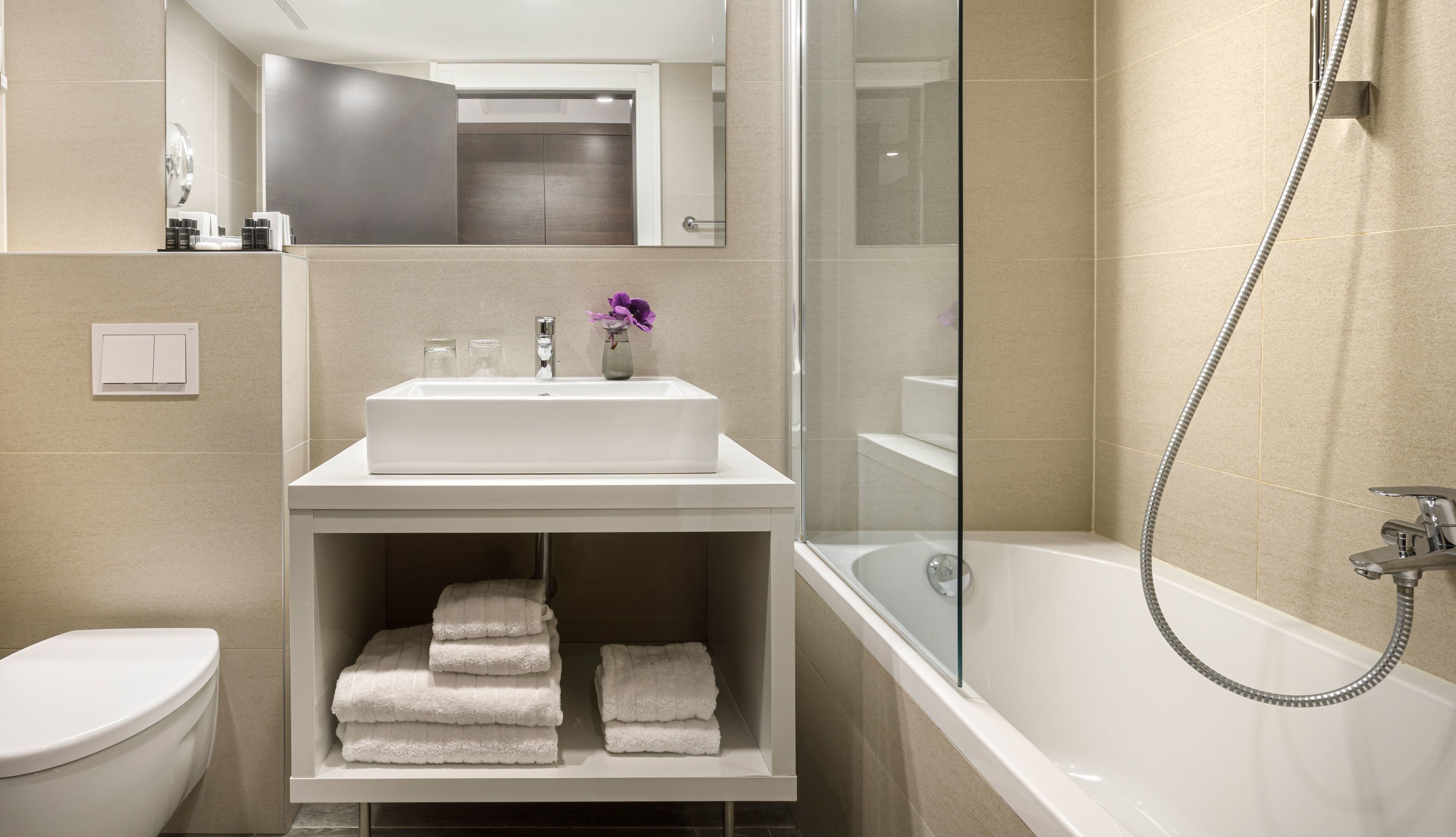 A modern bathroom with a white sink, a glass-enclosed shower, and a toilet.