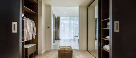 A modern walk-in closet with ample storage, a bench, and a view into a bright room.