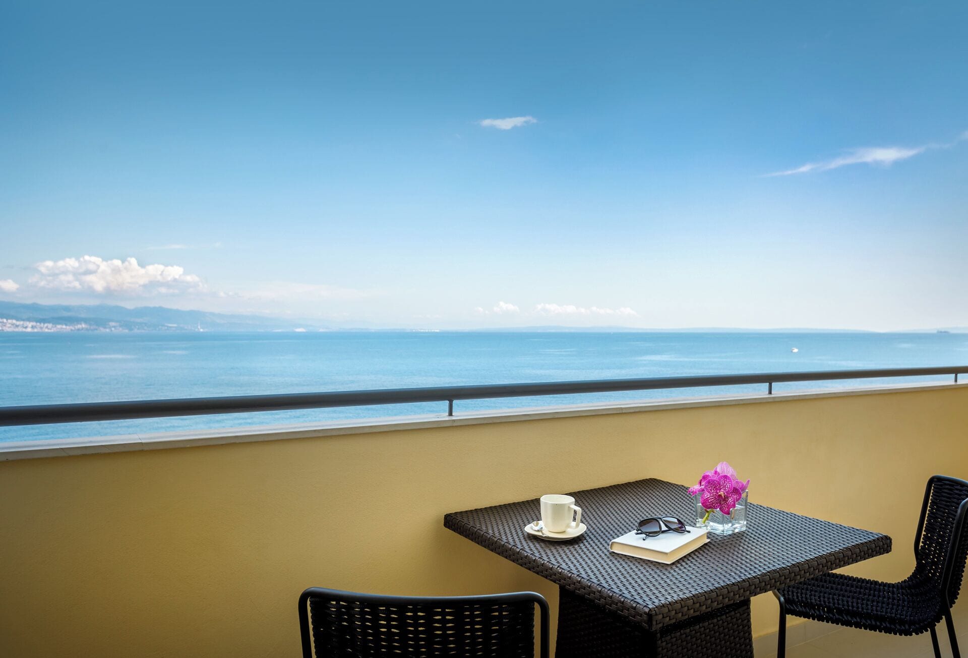 A balcony with a table, chairs, and a view of the sea.