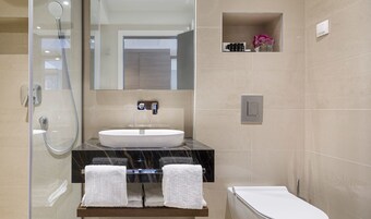 A modern bathroom with a glass-enclosed shower, a marble countertop, a white sink, and a built-in shelf with toiletries.