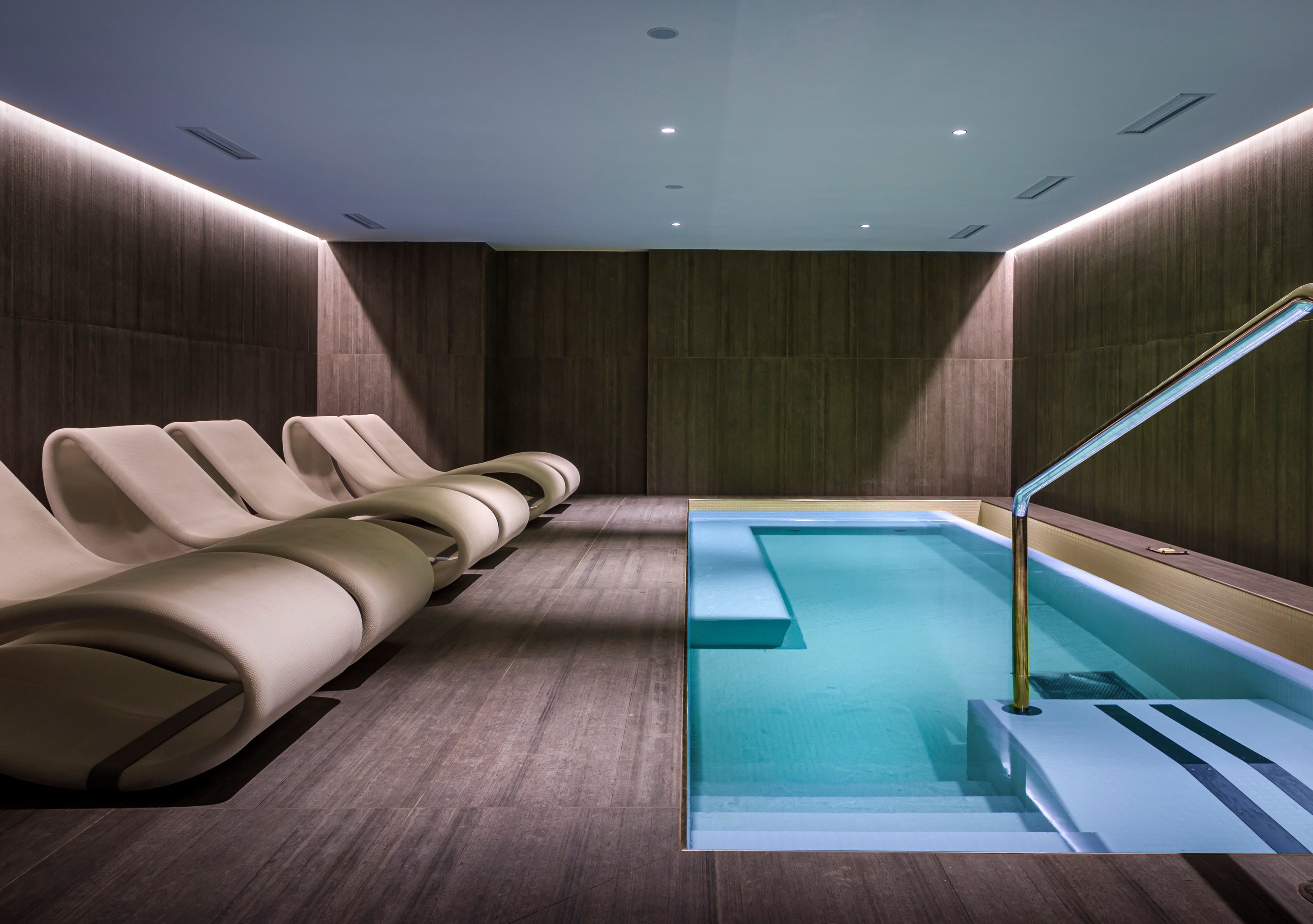 Moderni spa-alue, jossa on uima-allas, aurinkotuoleja ja puuseinästä tehty koristeellinen seinä.