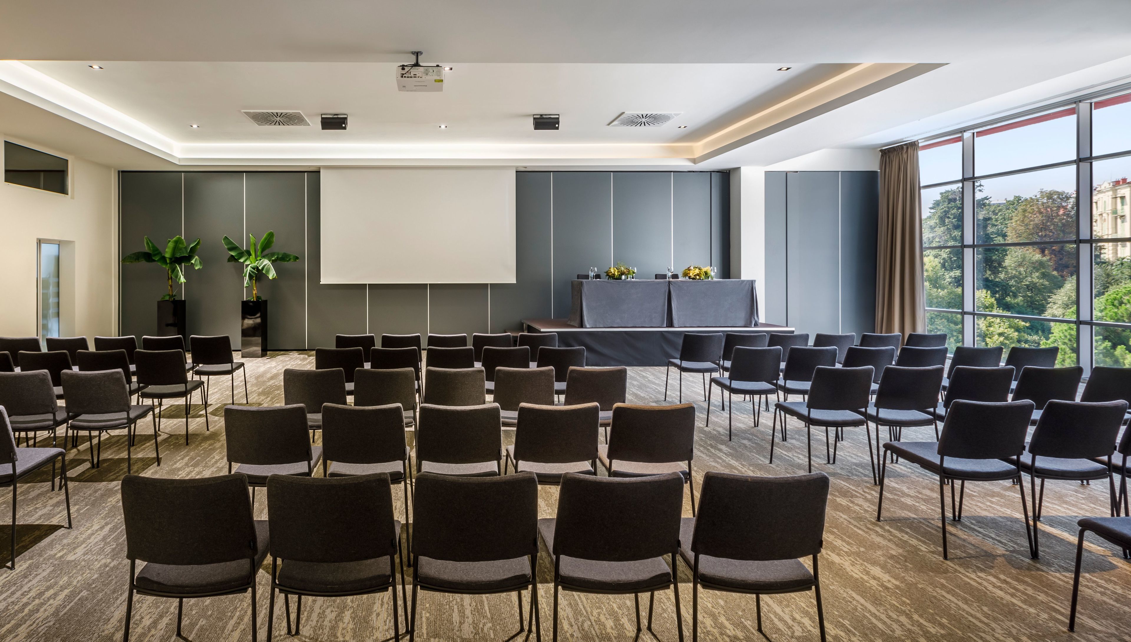 Ein Konferenzraum mit Reihen von Stühlen, einer Projektionsleinwand und einem Tisch mit Tischdecke.