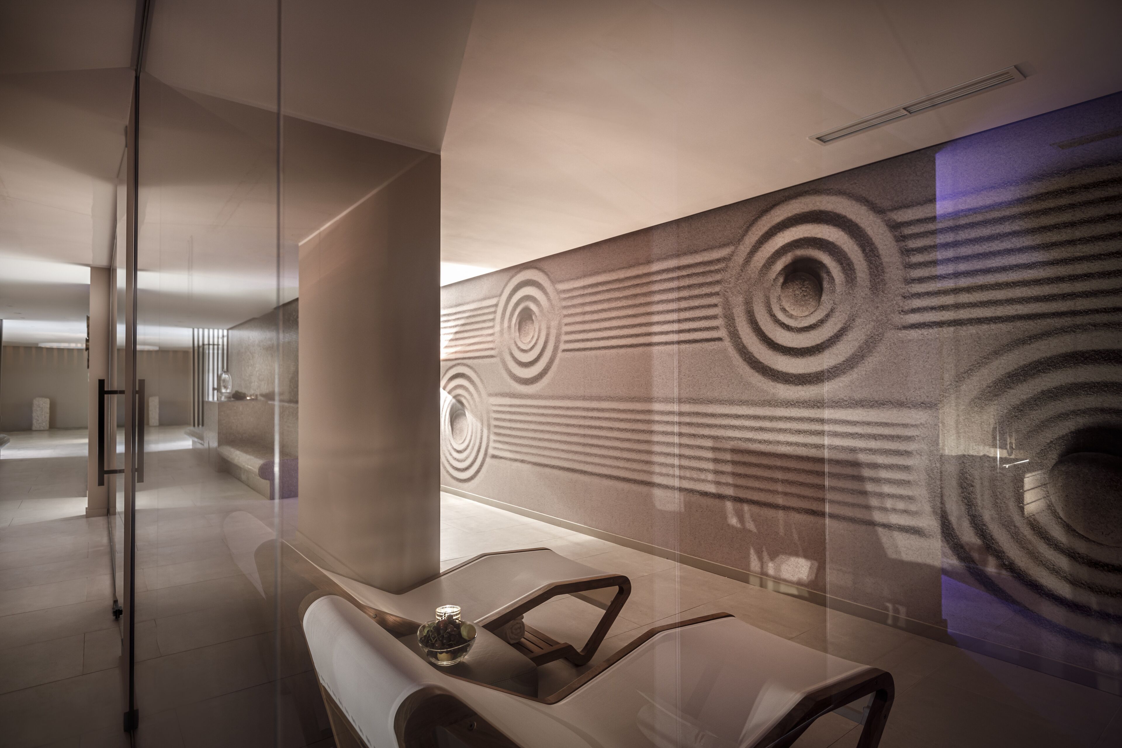 A modern interior with a minimalist design, featuring a glass partition, a seating area with a table, and a patterned wall.