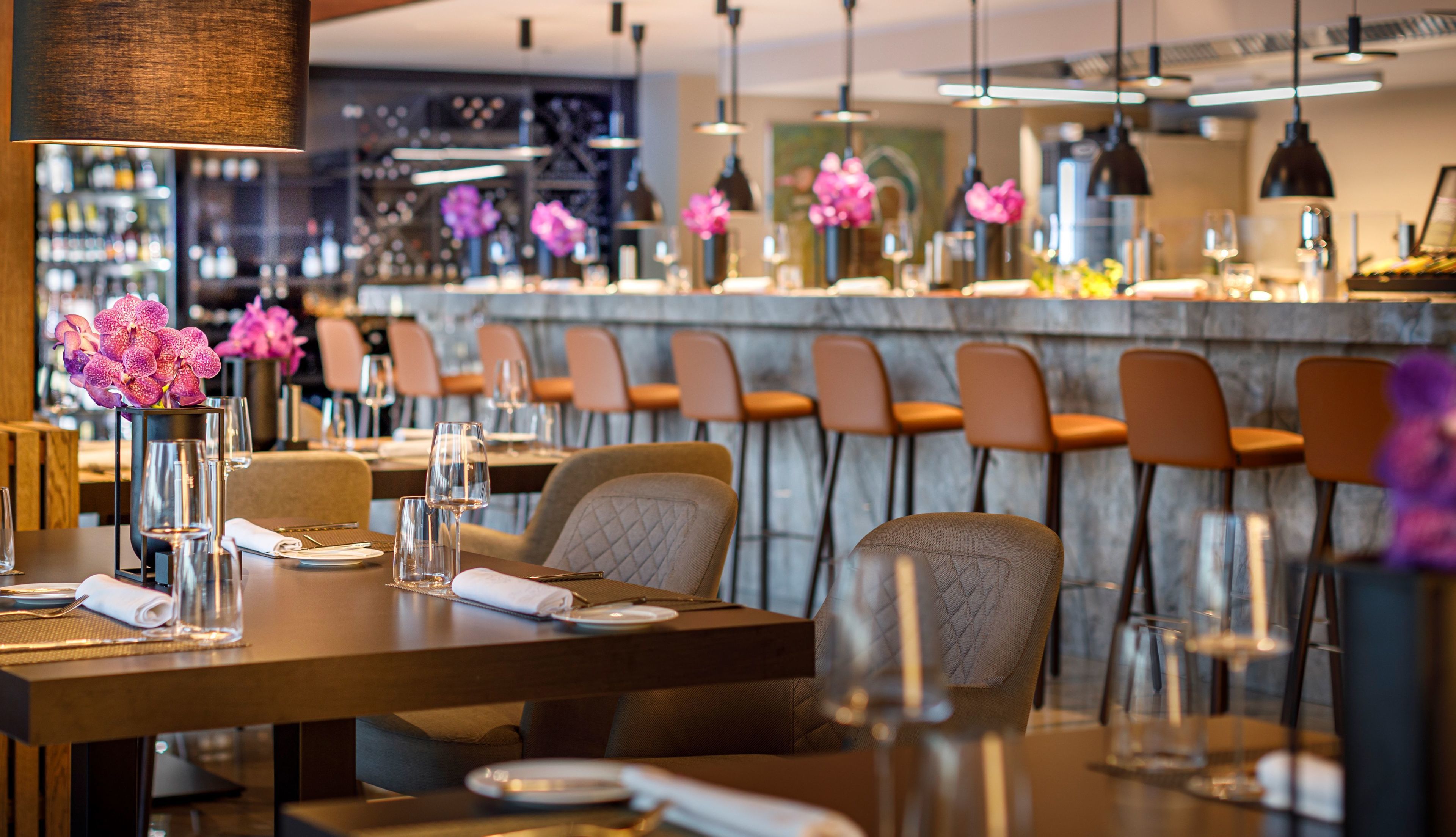Un restaurant doté d'un bar, de tabourets et de tables dressées avec des verres à vin et des serviettes.