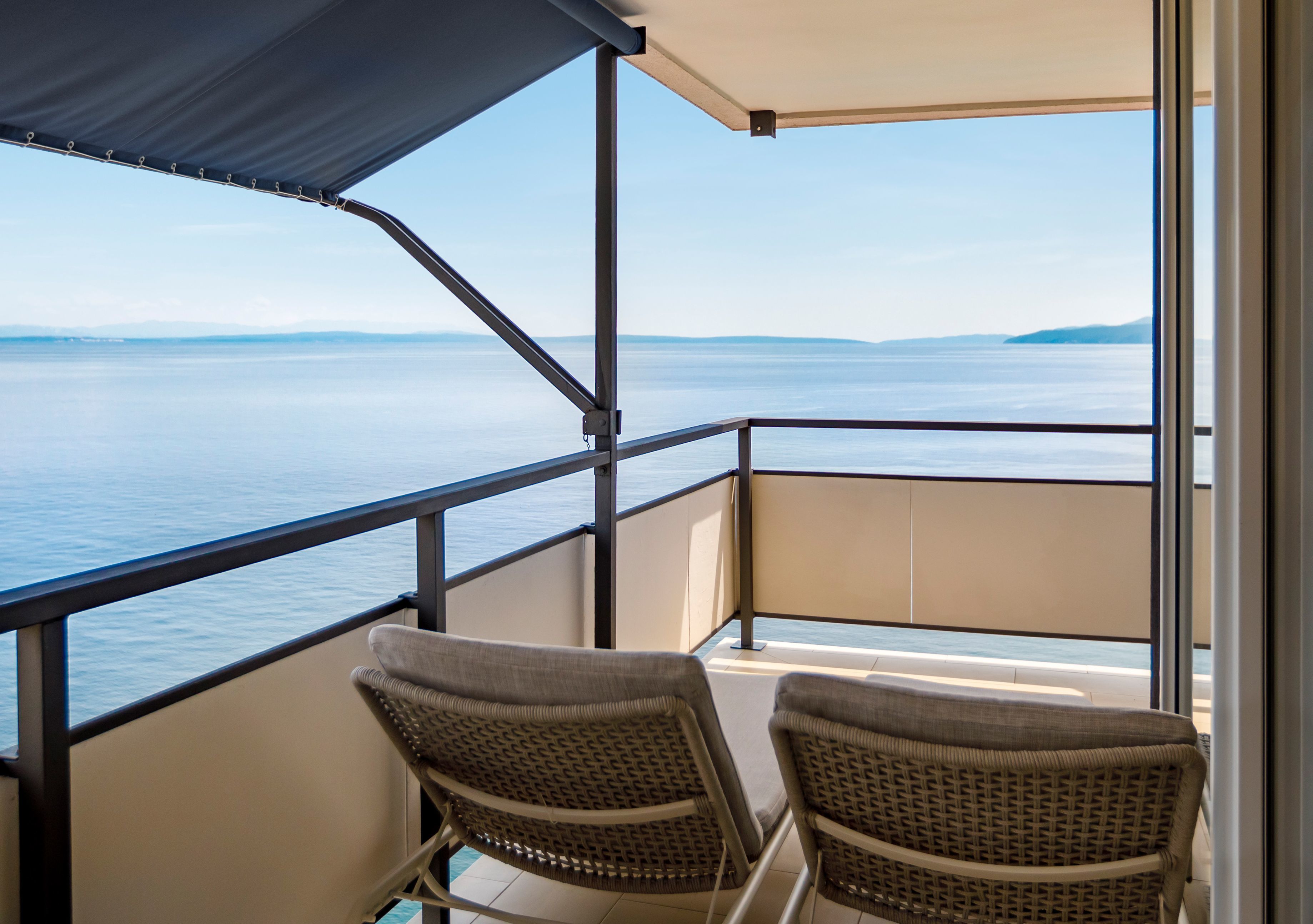 A balcony with two wicker chairs, a metal railing, and a view of the sea.