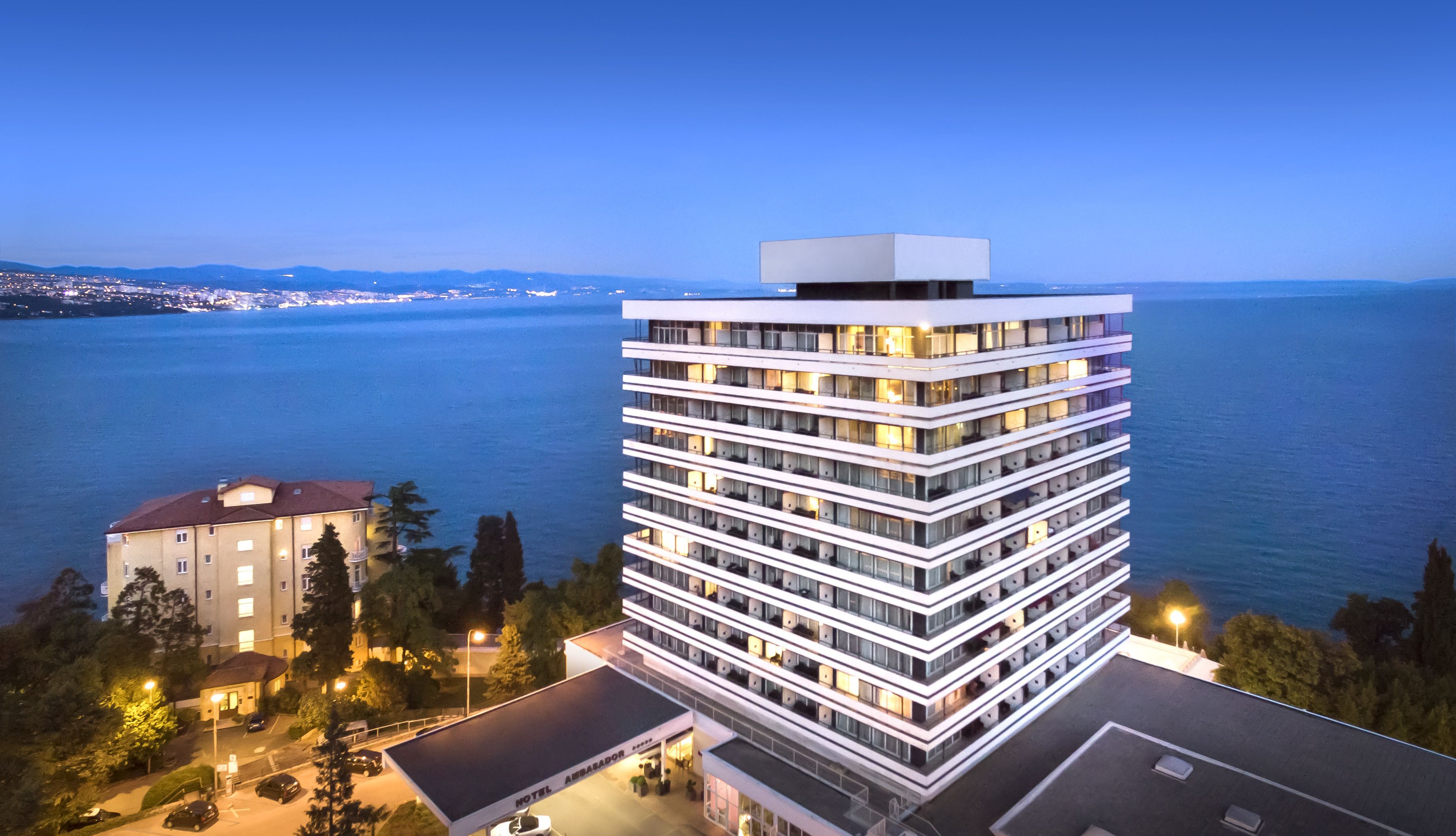 A modern hotel with multiple floors, a flat roof, and a view of the sea.