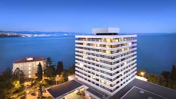 A modern hotel with multiple floors, a flat roof, and a view of the sea.