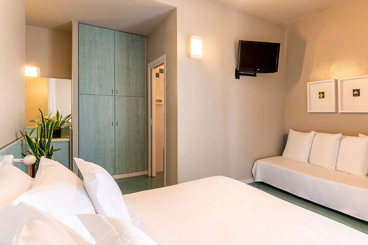 Camera d'albergo con un letto, una divisa, un armadio, una TV e uno specchio.