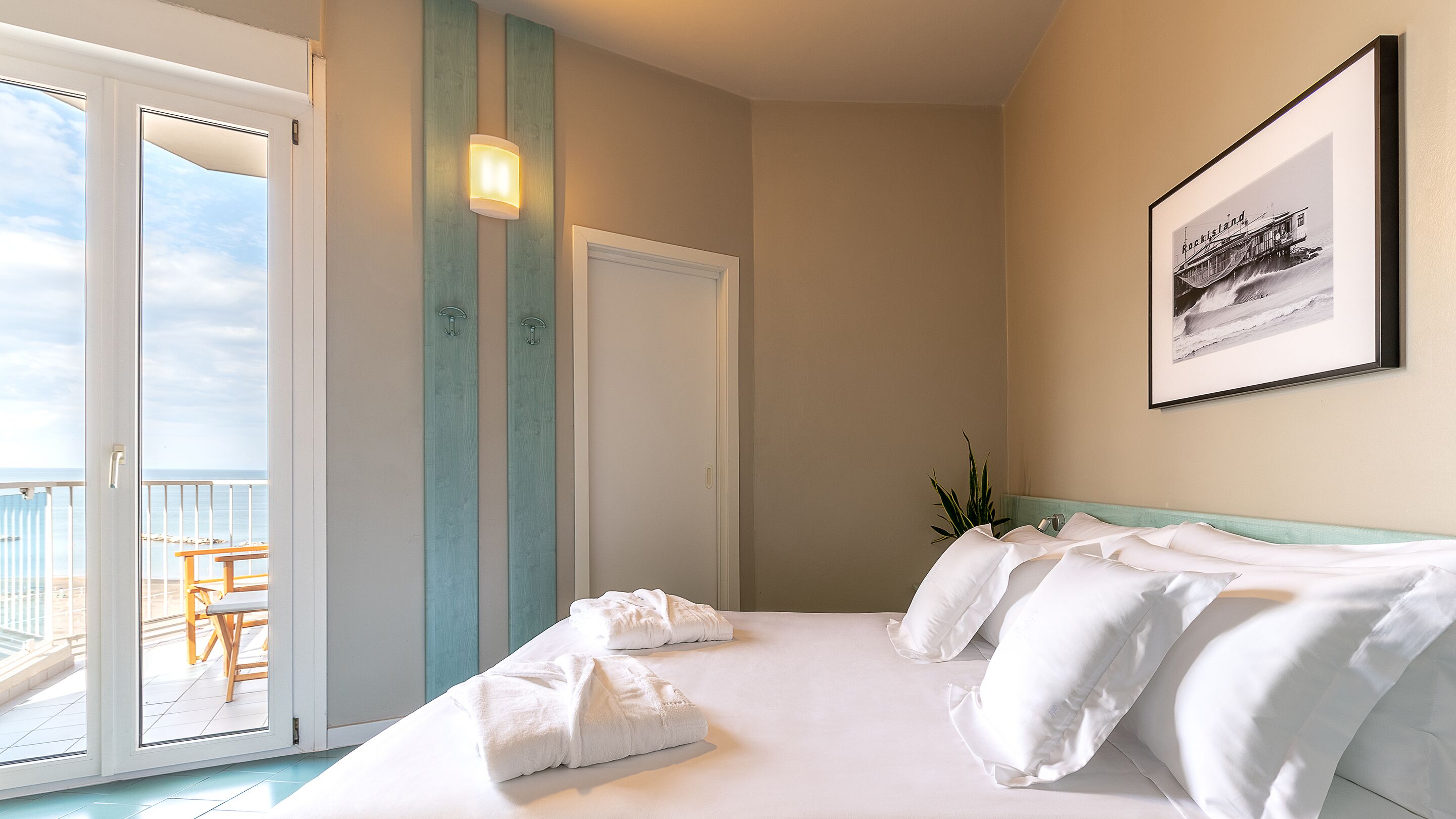 Habitación de hotel con cama, balcón, puerta y un cuadro en la pared.