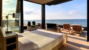 A modern bedroom with a large bed, a TV, and a balcony with chairs and a view of the sea. - Victoria Palace Hotel (Cattolica)