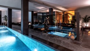 A modern indoor pool area with glass walls, a lounge area, and a bar. - Victoria Palace Hotel (Cattolica)