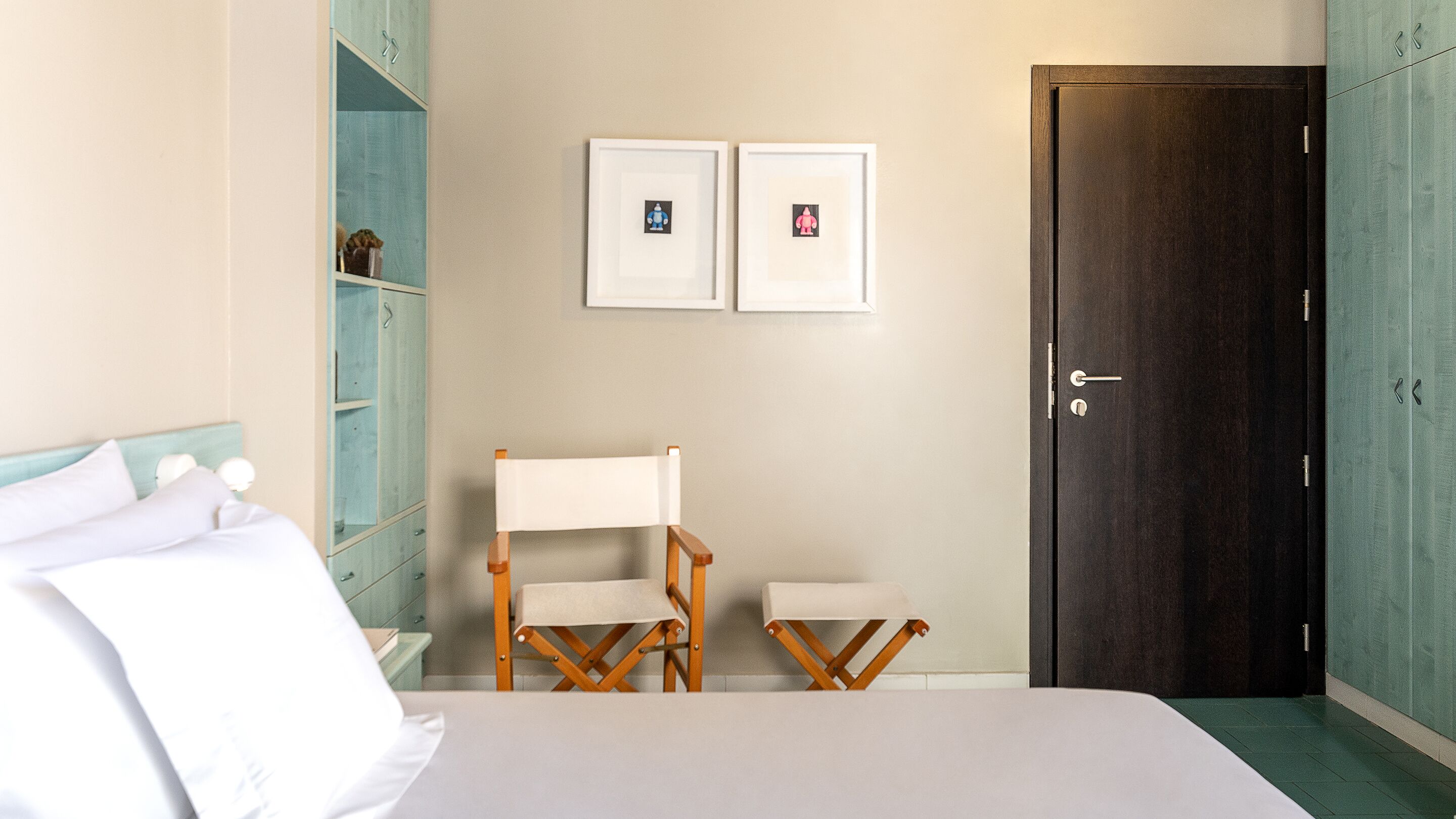 Una habitación de hotel con cama, dos sillones, un armario y dos cuadros en la pared.