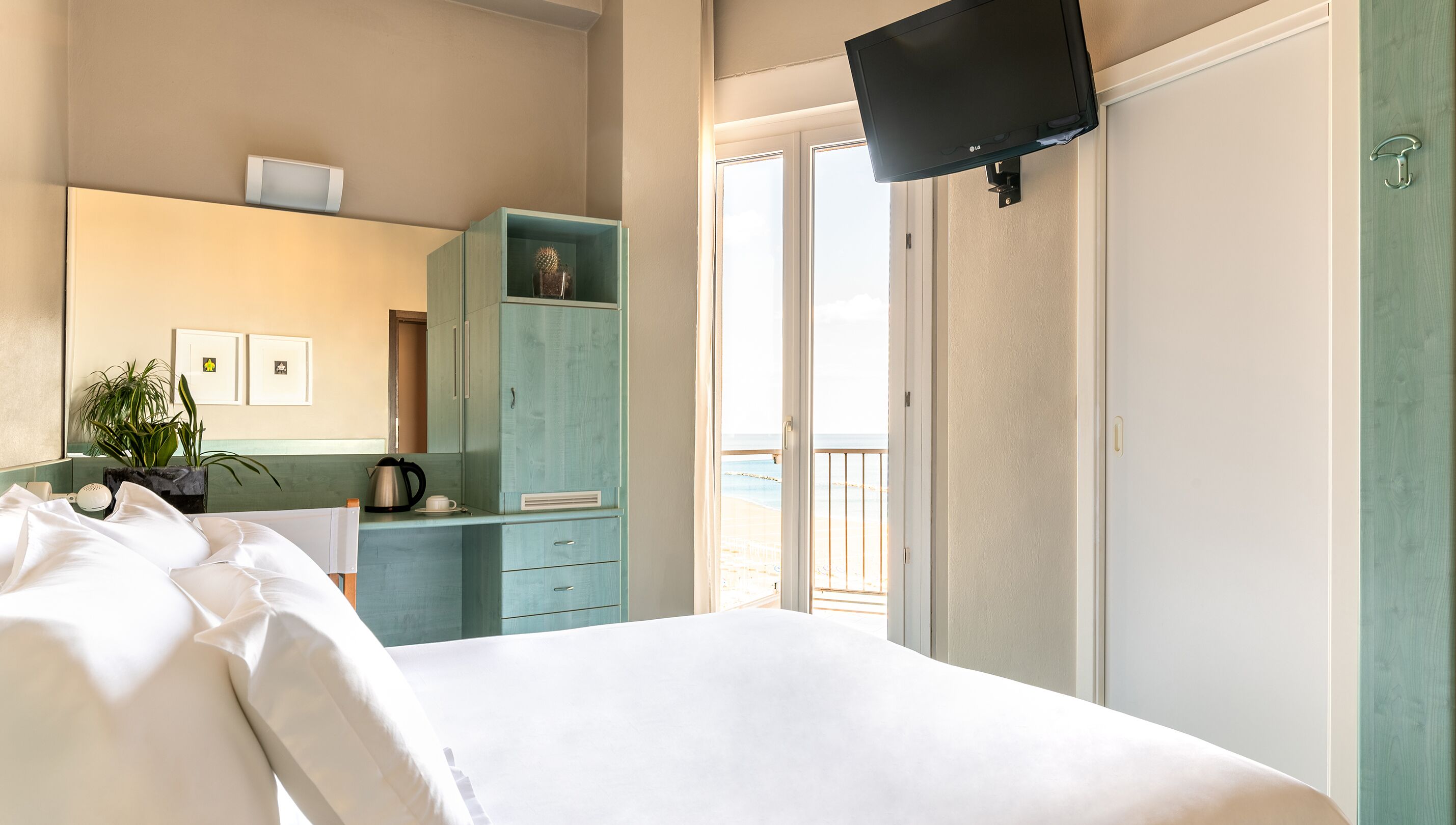 Un dormitorio con cama, televisor montado en la pared, cómoda y vista a la playa a través de una puerta corrediza.
