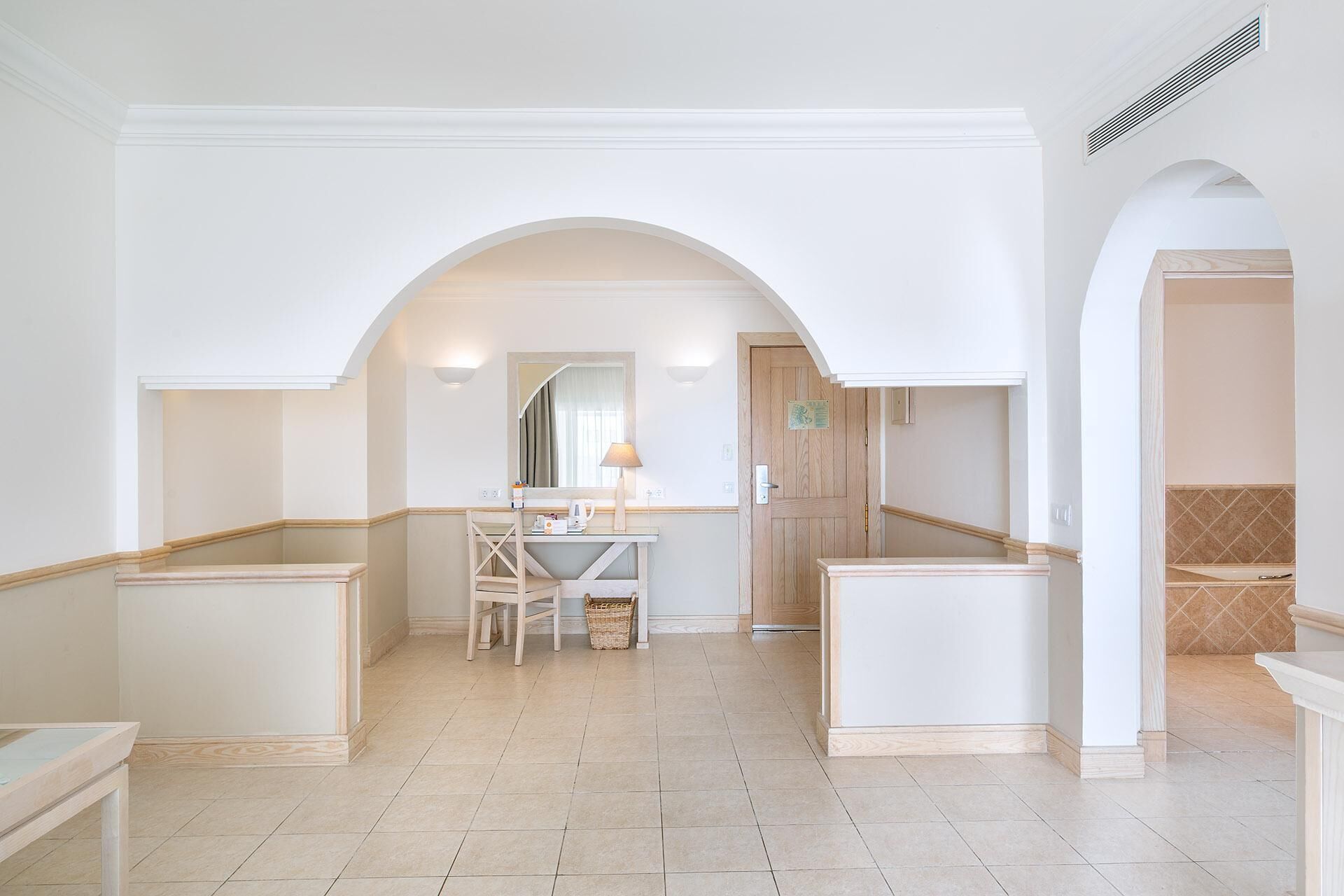 A spacious hallway with a central seating area, a wooden door, and a tiled floor.