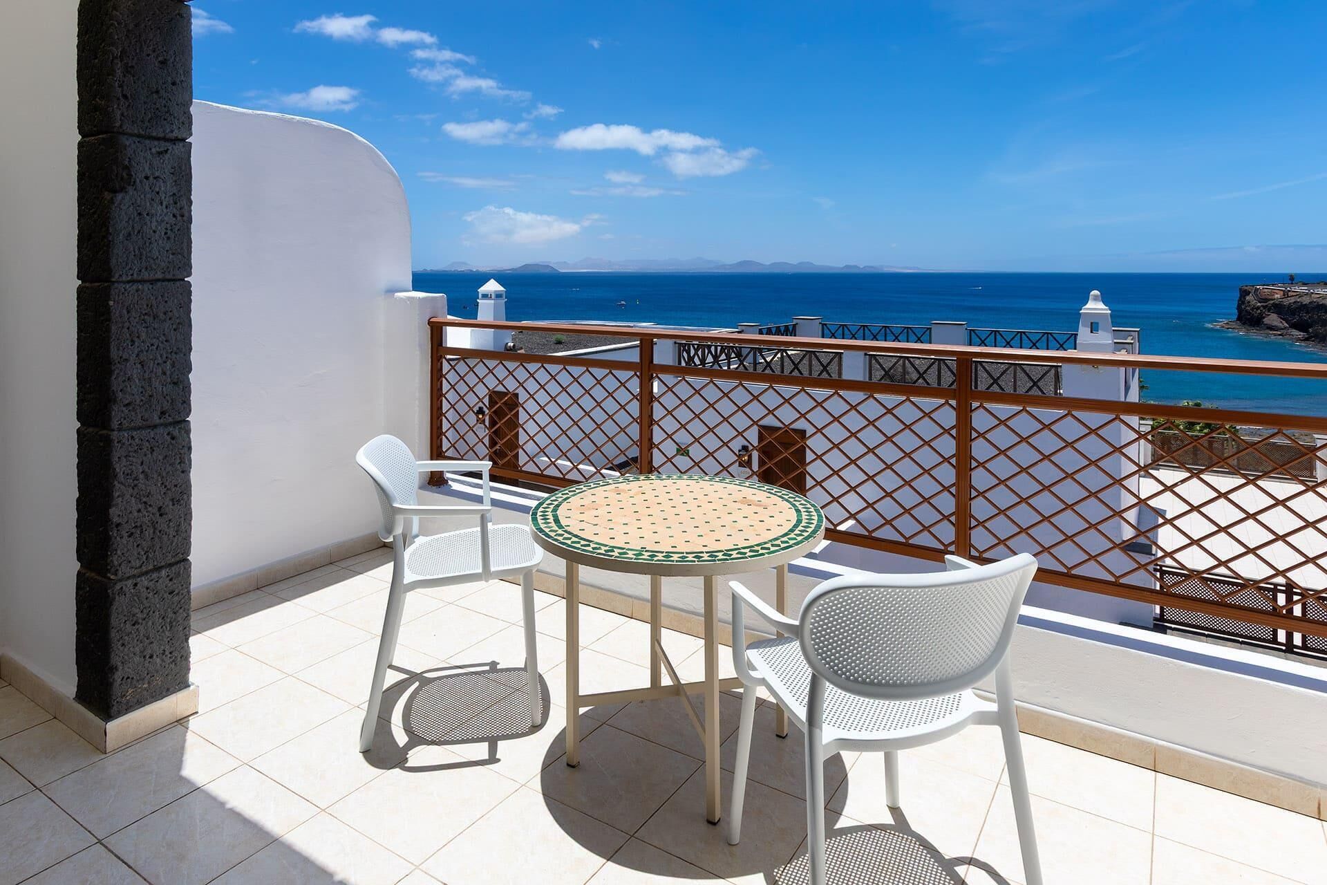 Un balcón con una mesa redonda y dos sillas, con vistas a la costa, edificios y al mar.