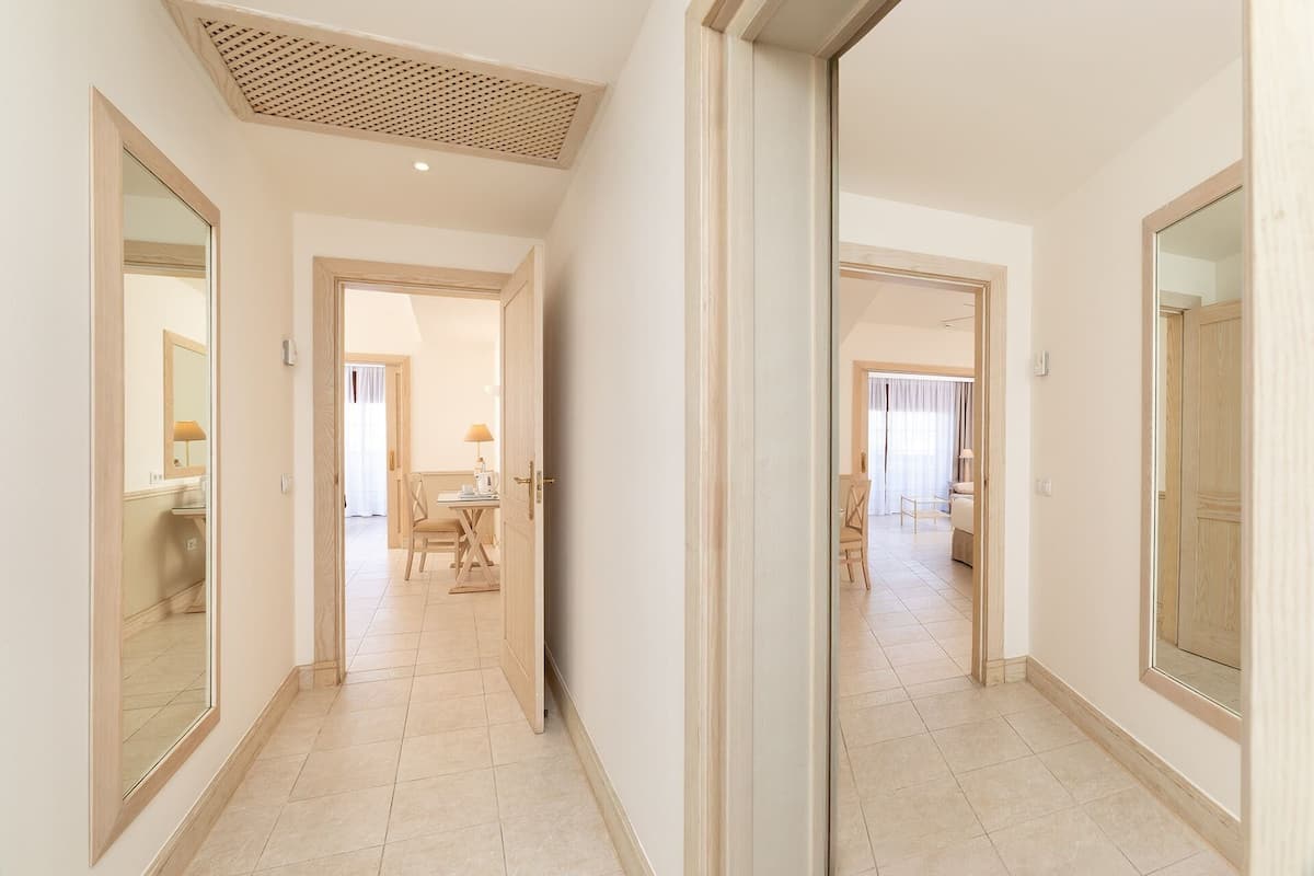 A hallway with a mirrored wall, leading to a dining area with a table and chairs.