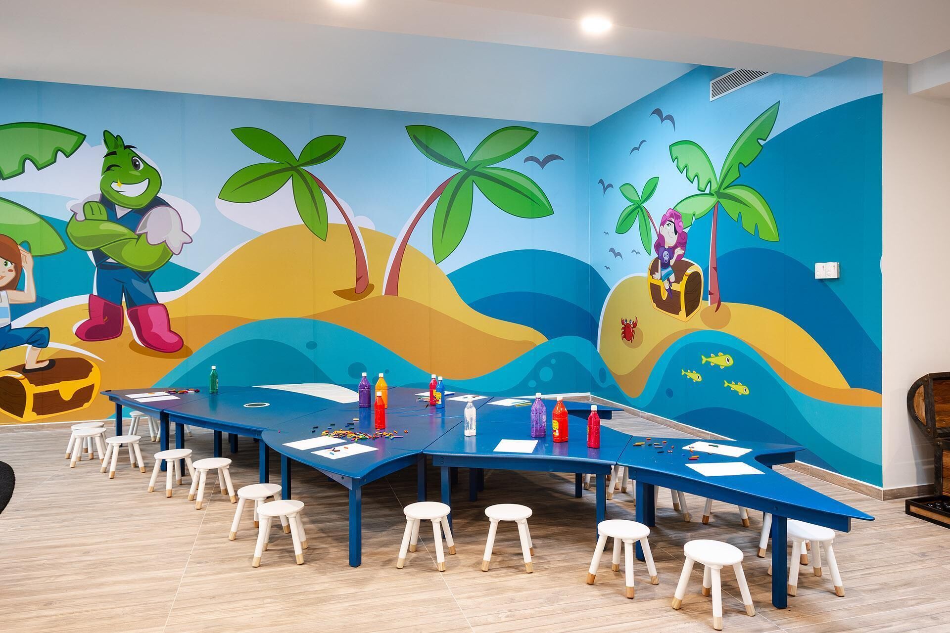 A conference room with a colorful mural depicting a beach scene, a long table with chairs, and various items on the table.