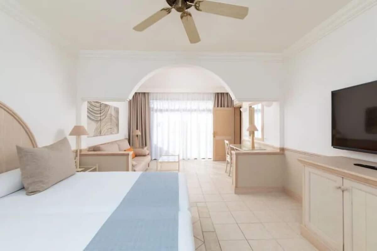 A hotel room with a large bed, a desk, a television, and a ceiling fan.