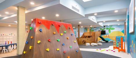 Un área infantil con pared de escalada, tobogán y casita.