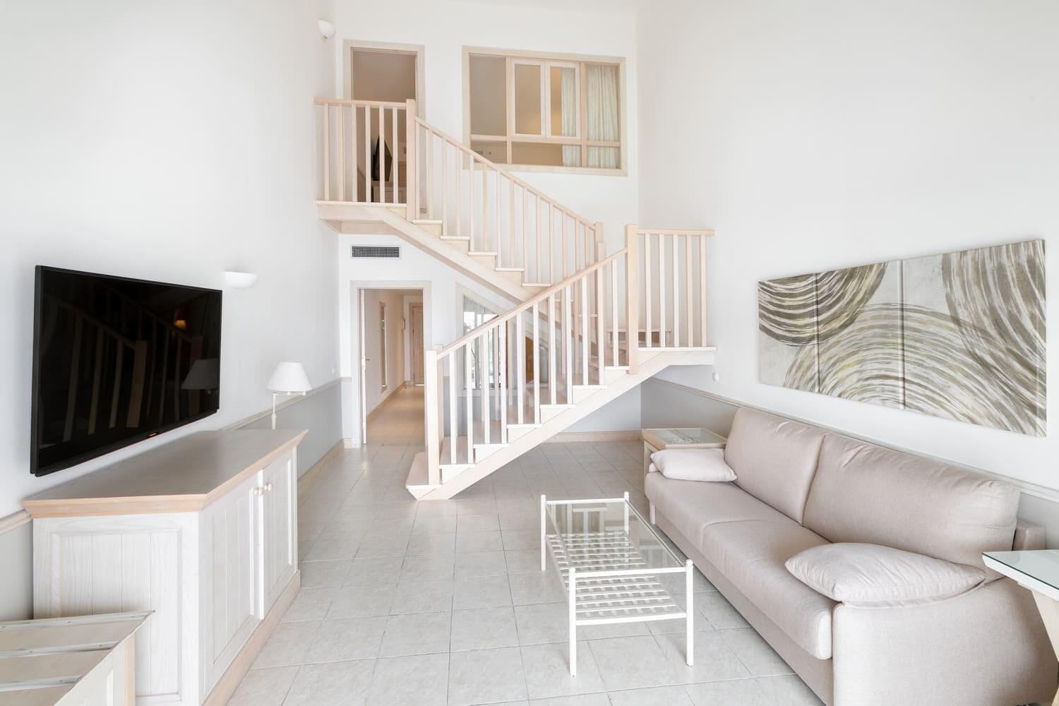Una sala de estar moderna con una televisión de pantalla plana, un sofá, una mesa de centro y una escalera.