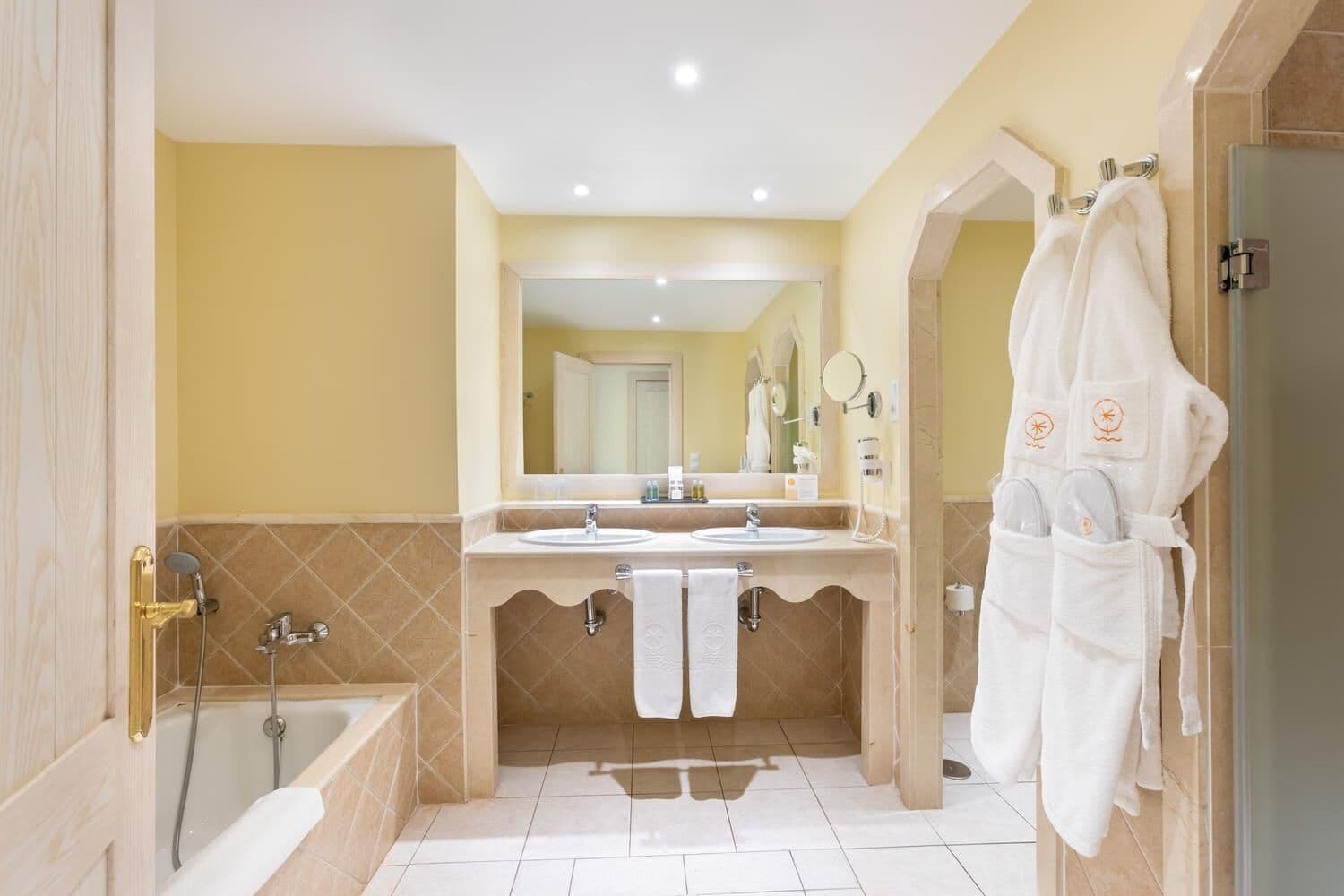 A modern bathroom with a bathtub, two sinks, a large mirror, and a robe hanging on a hook.