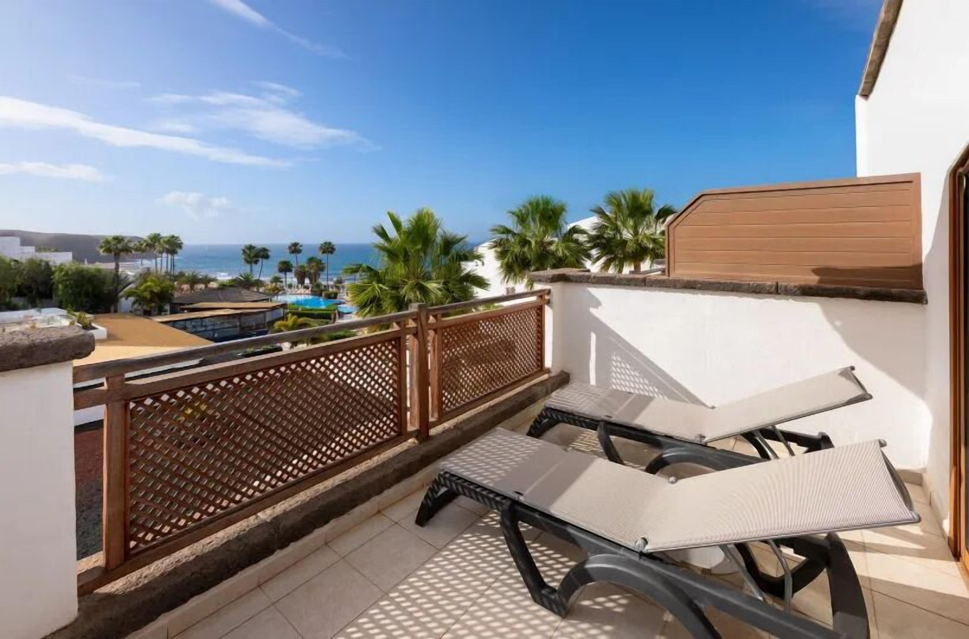 Un balcon avec vue sur l’océan, une piscine et des palmiers.