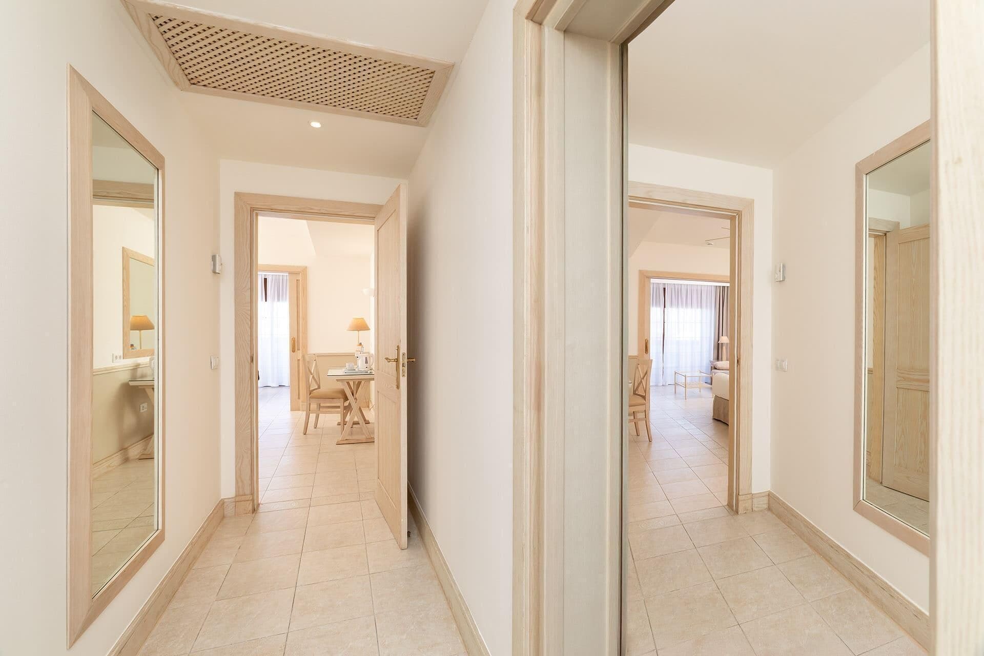 A hallway with a mirrored wall, leading to a dining area with a table and chairs.