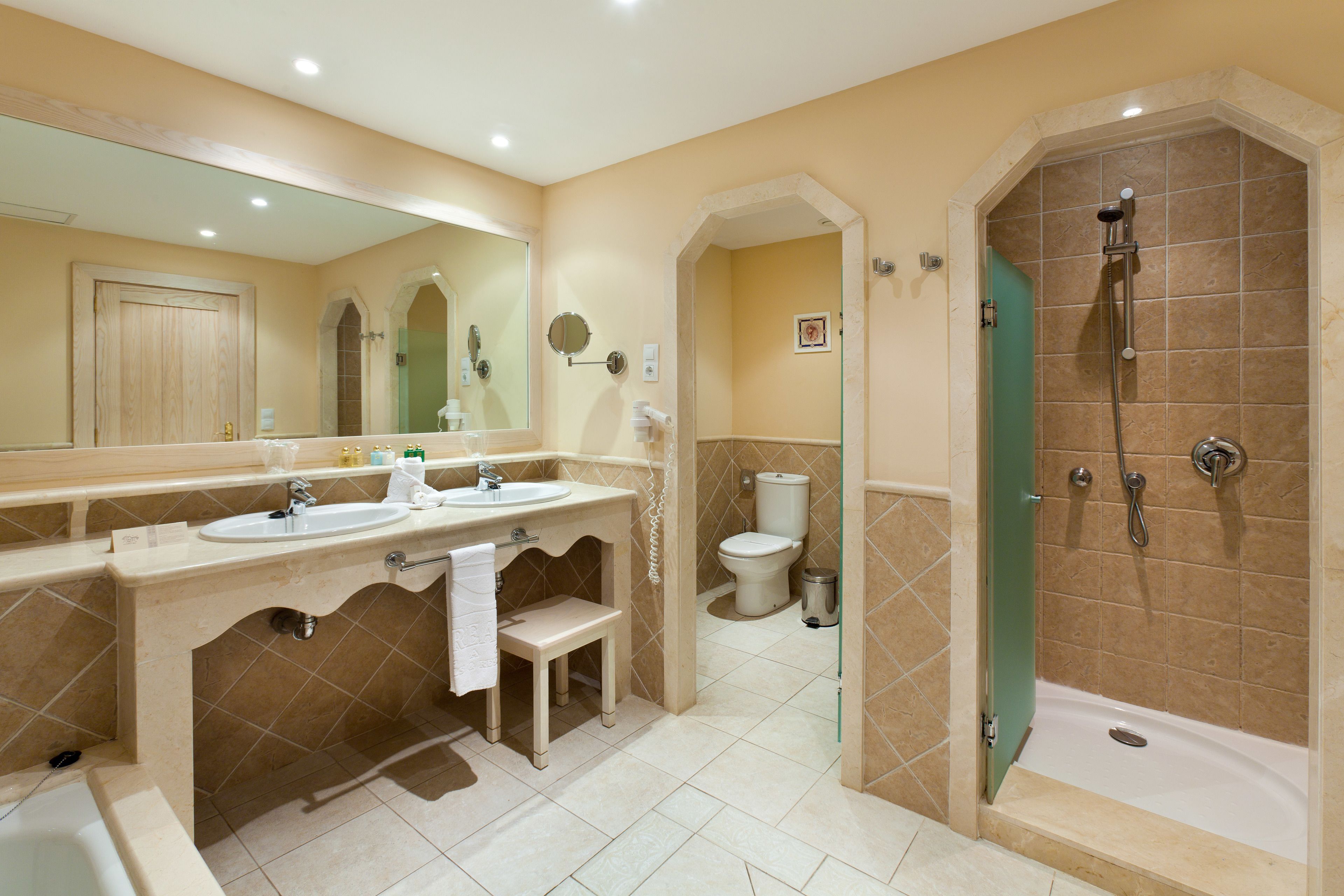 A bathroom with two sinks, a mirror, a toilet, and a shower.