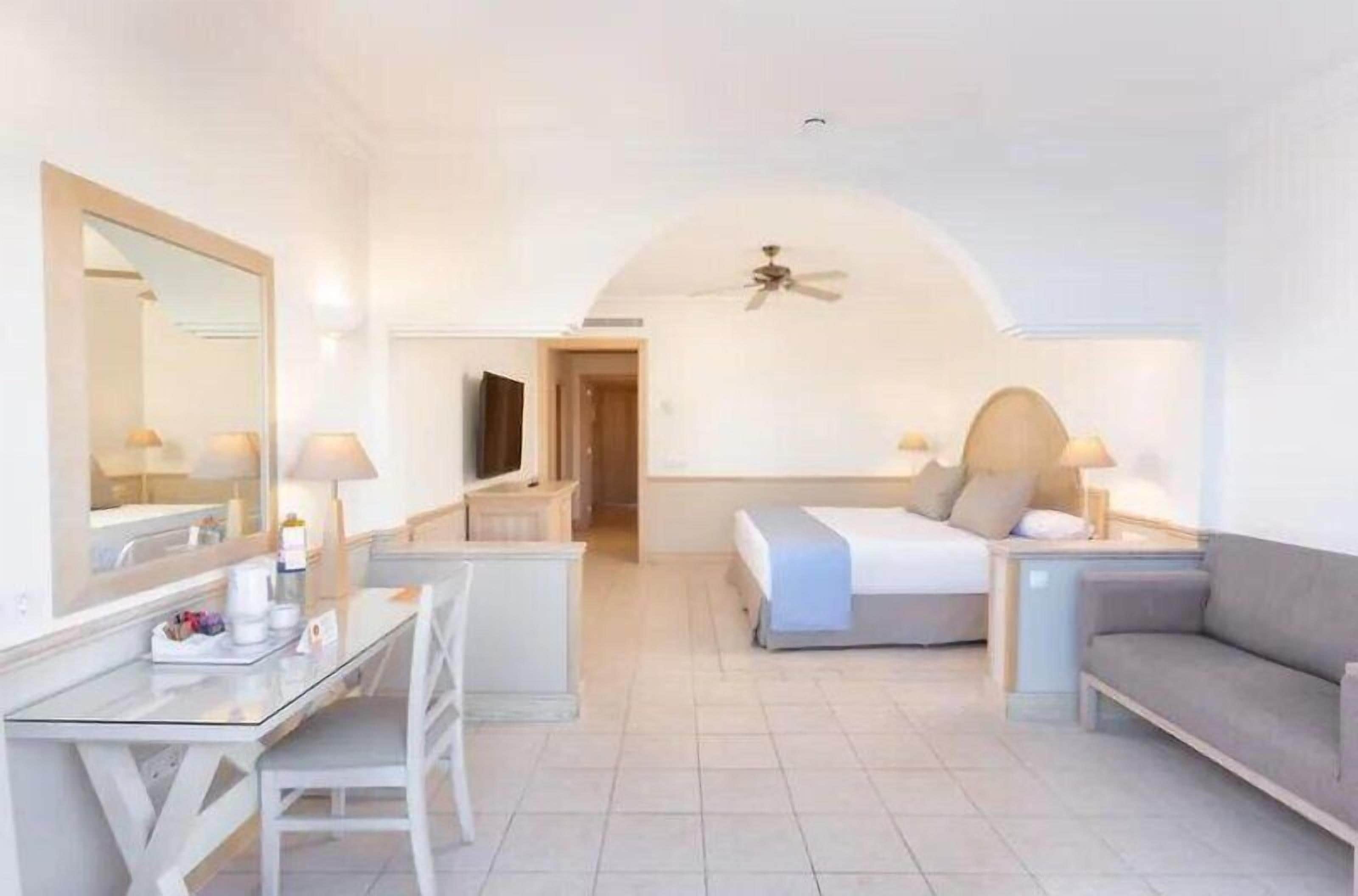 A hotel room with a bed, a desk, a chair, a sofa, and a TV.