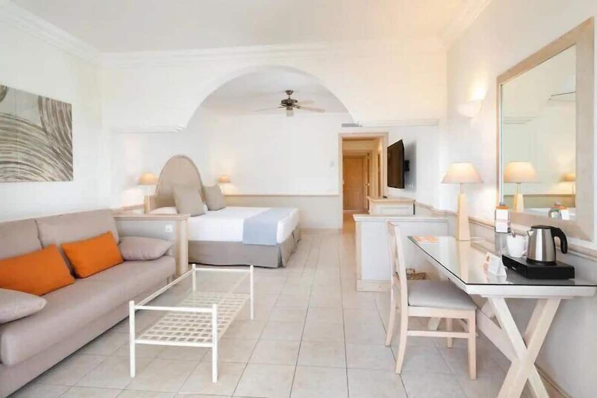 A modern hotel room with a sofa, bed, desk, and a large mirror.