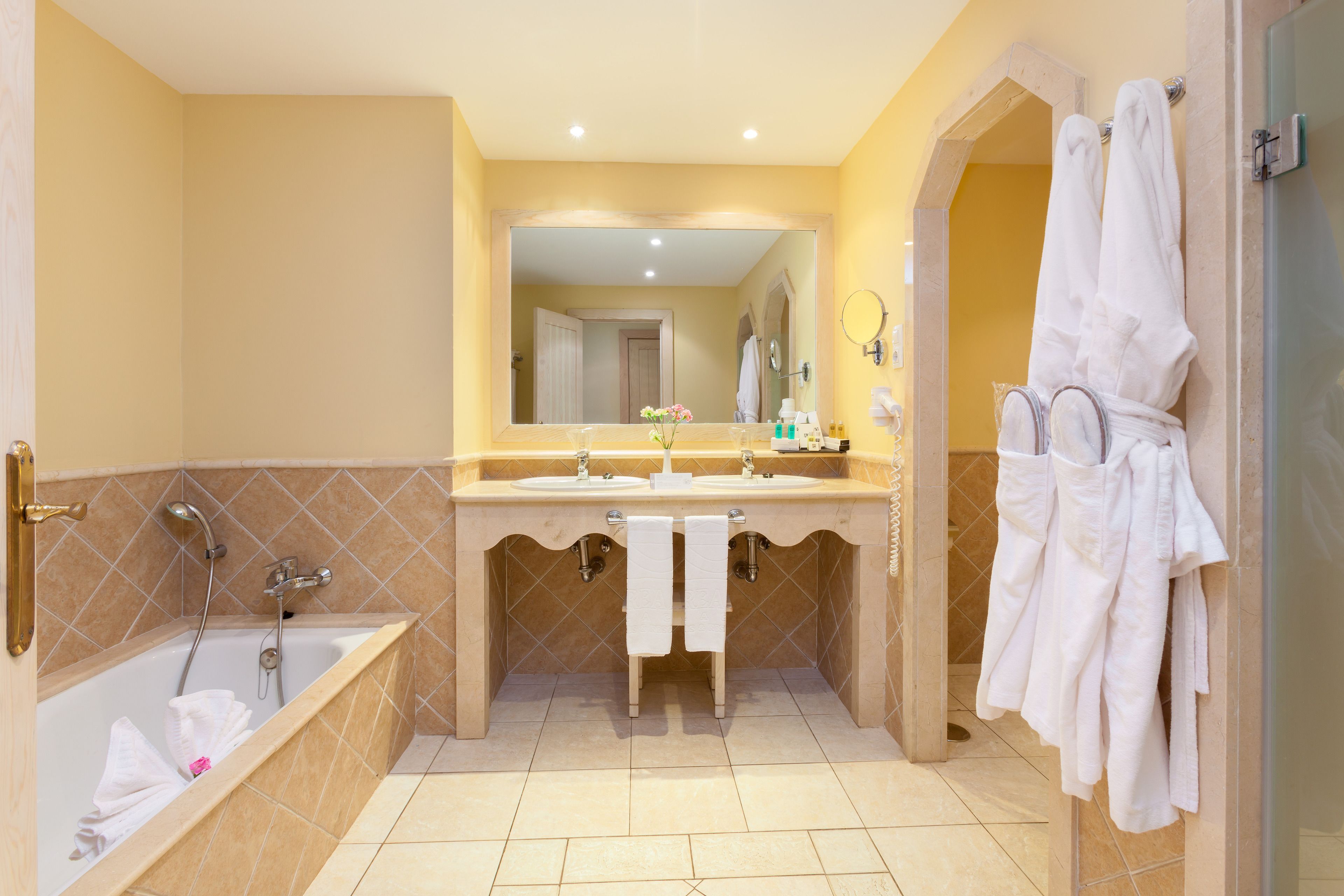 A bathroom with a bathtub, two sinks, a large mirror, and a shower area.