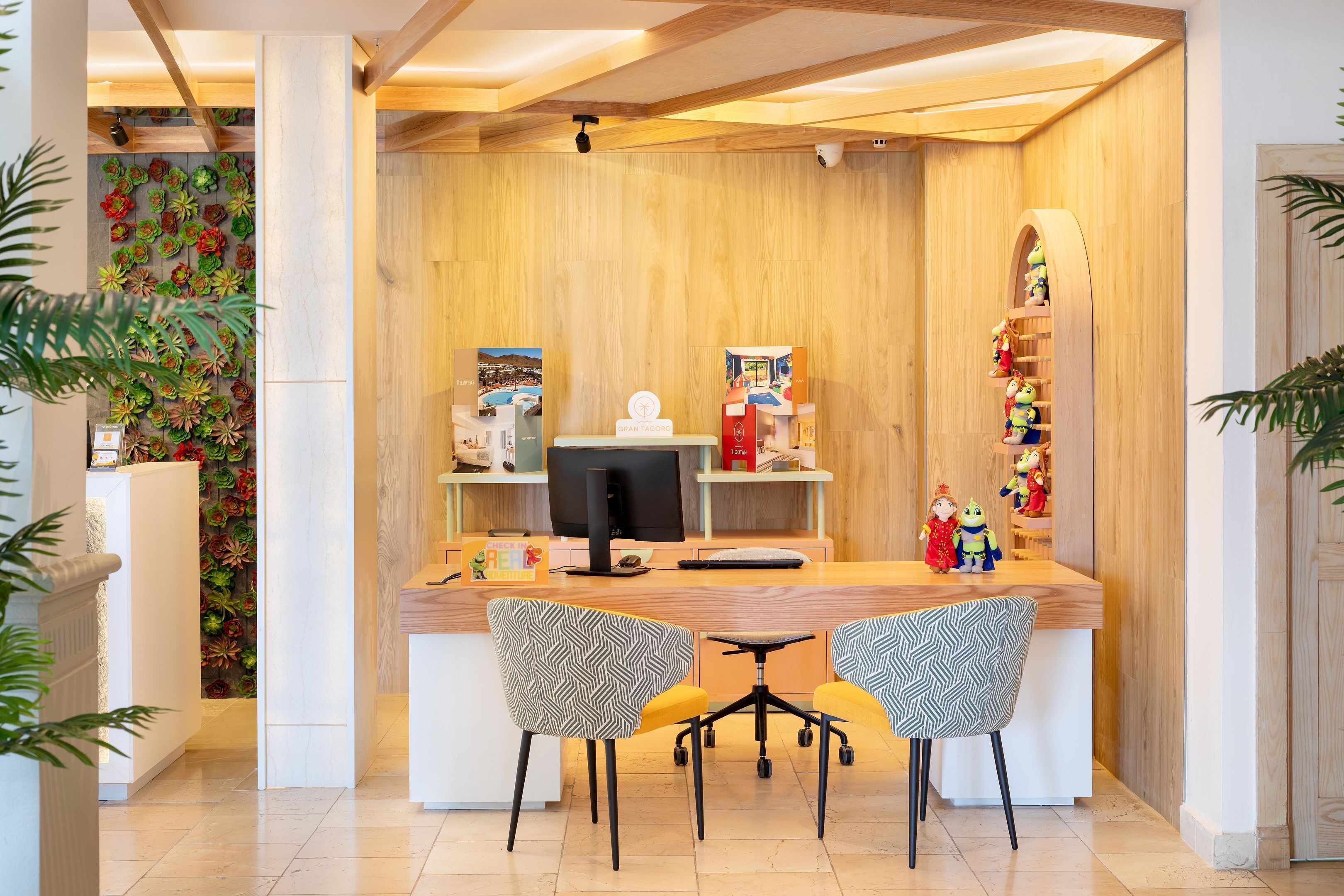 Een receptiegedeelte met een houten balie, twee stoelen, een computer en decoratieve objecten.