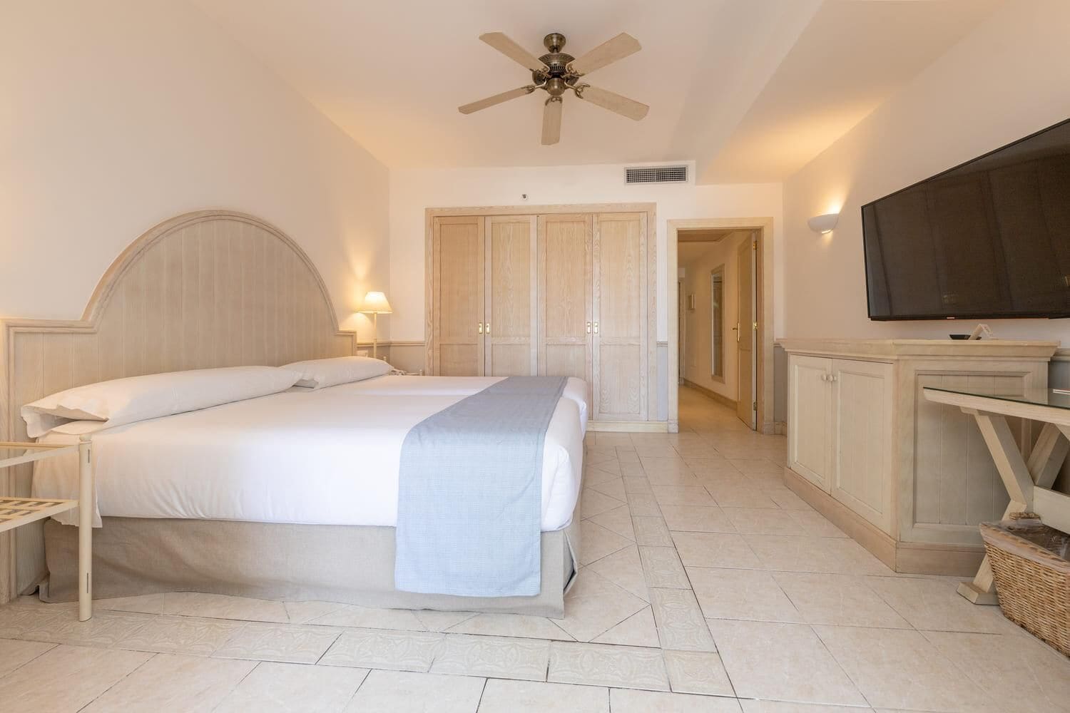 Una habitación de hotel con cama, televisión, ventilador de techo y armario.
