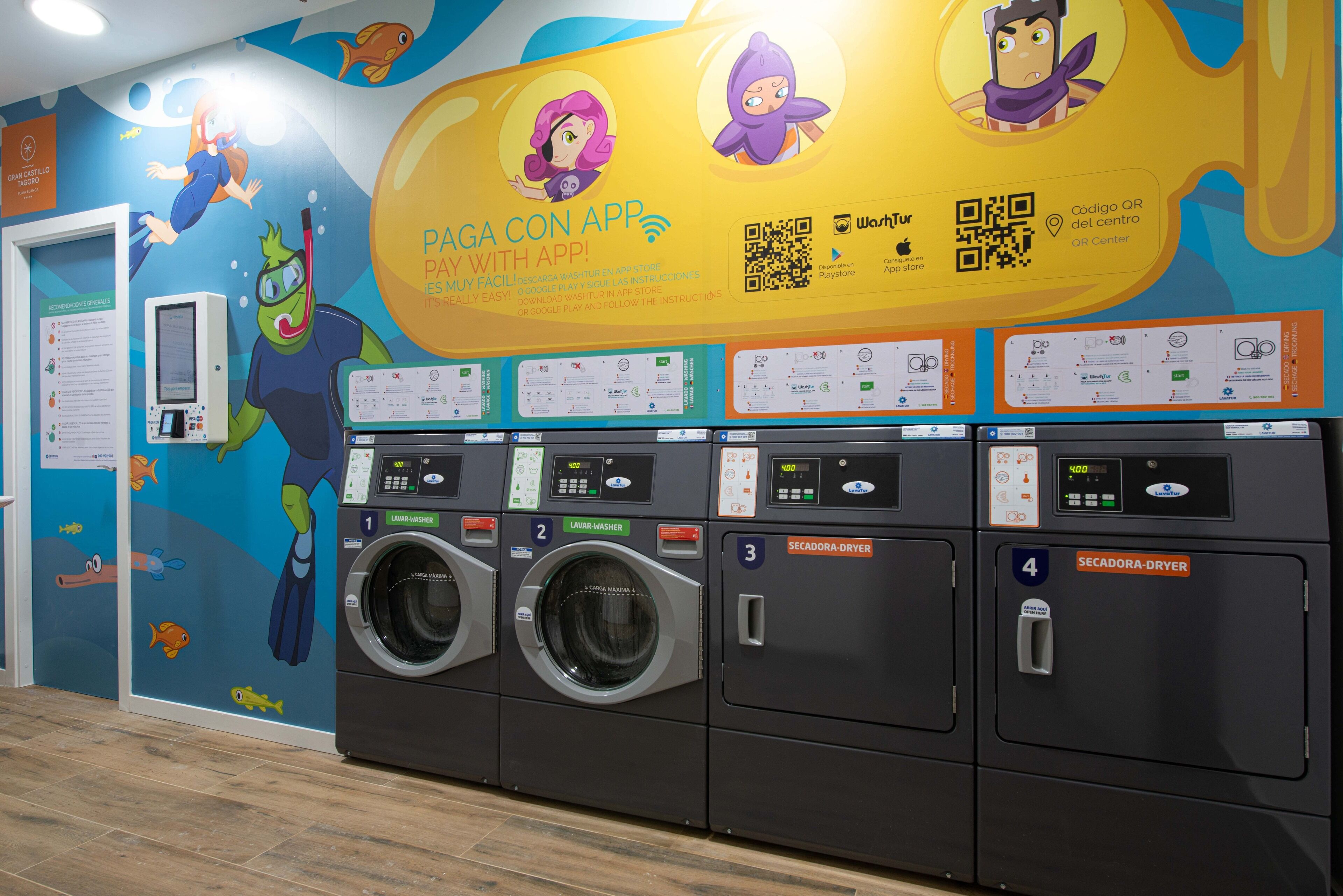 A laundromat with multiple washing machines and dryers, a QR code for app download, and colorful wall murals.