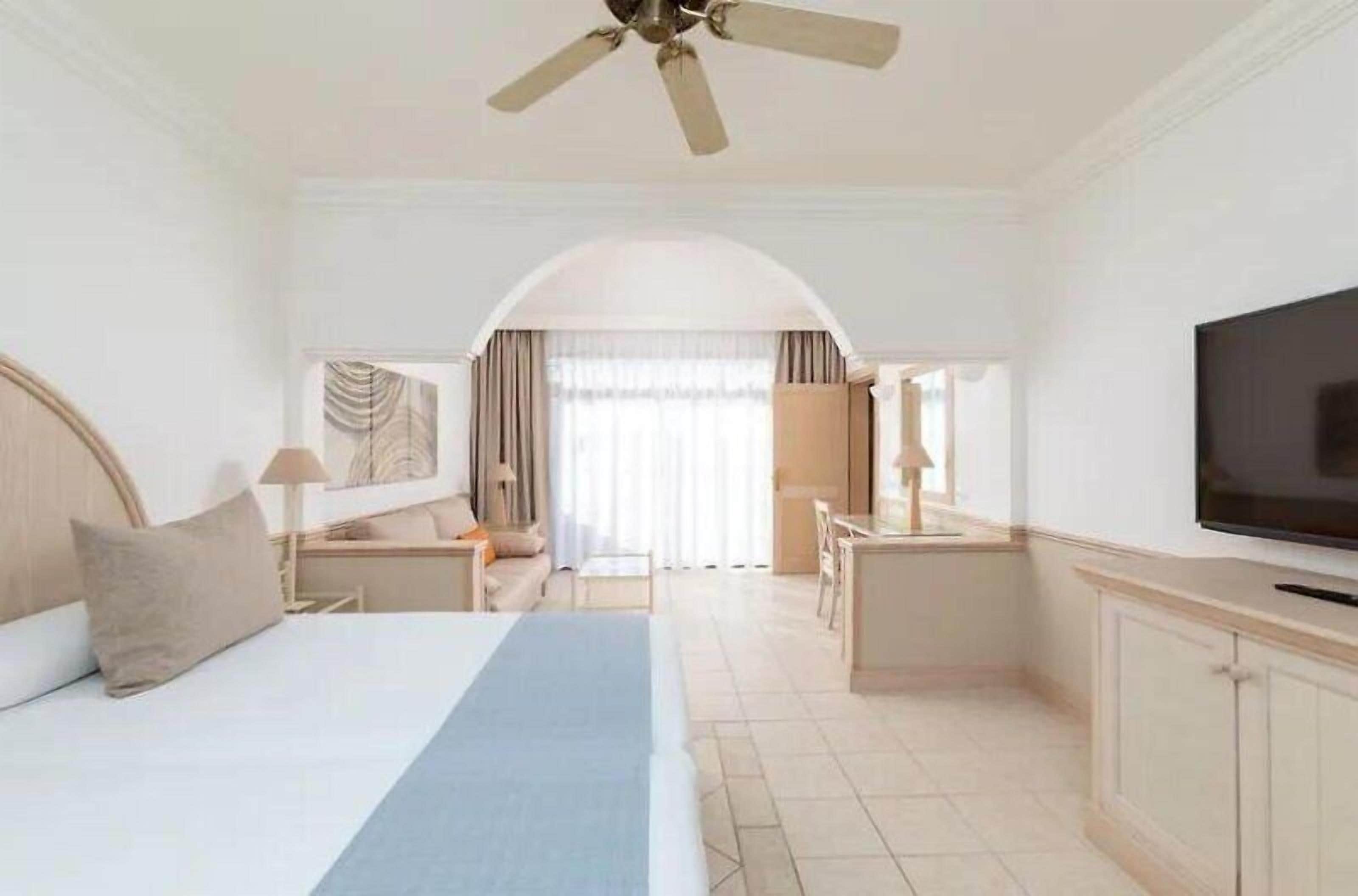 Habitación de hotel con cama, escritorio, televisor y vistas al exterior.