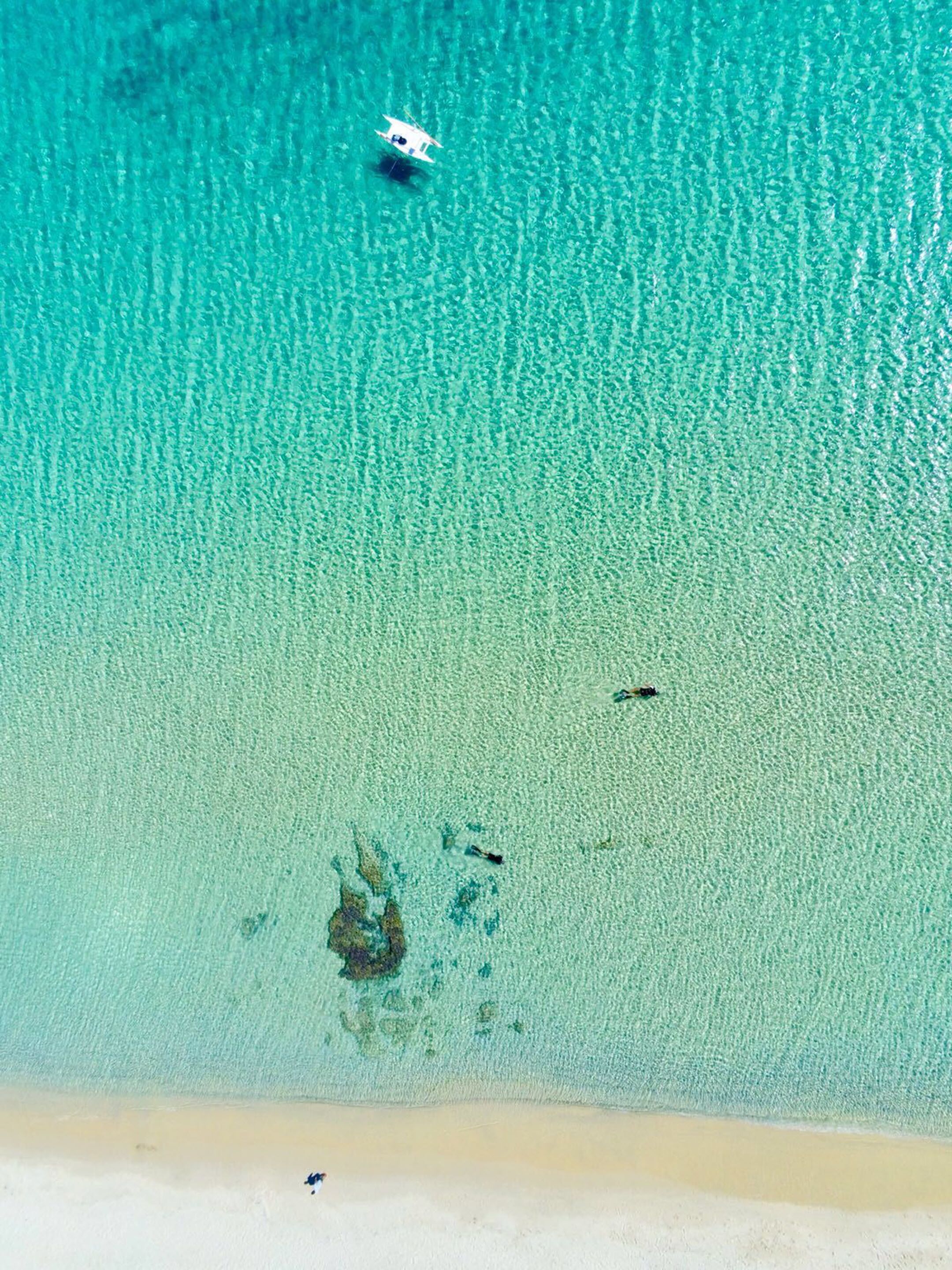 A clear turquoise sea with a sandy beach and a small boat in the distance.