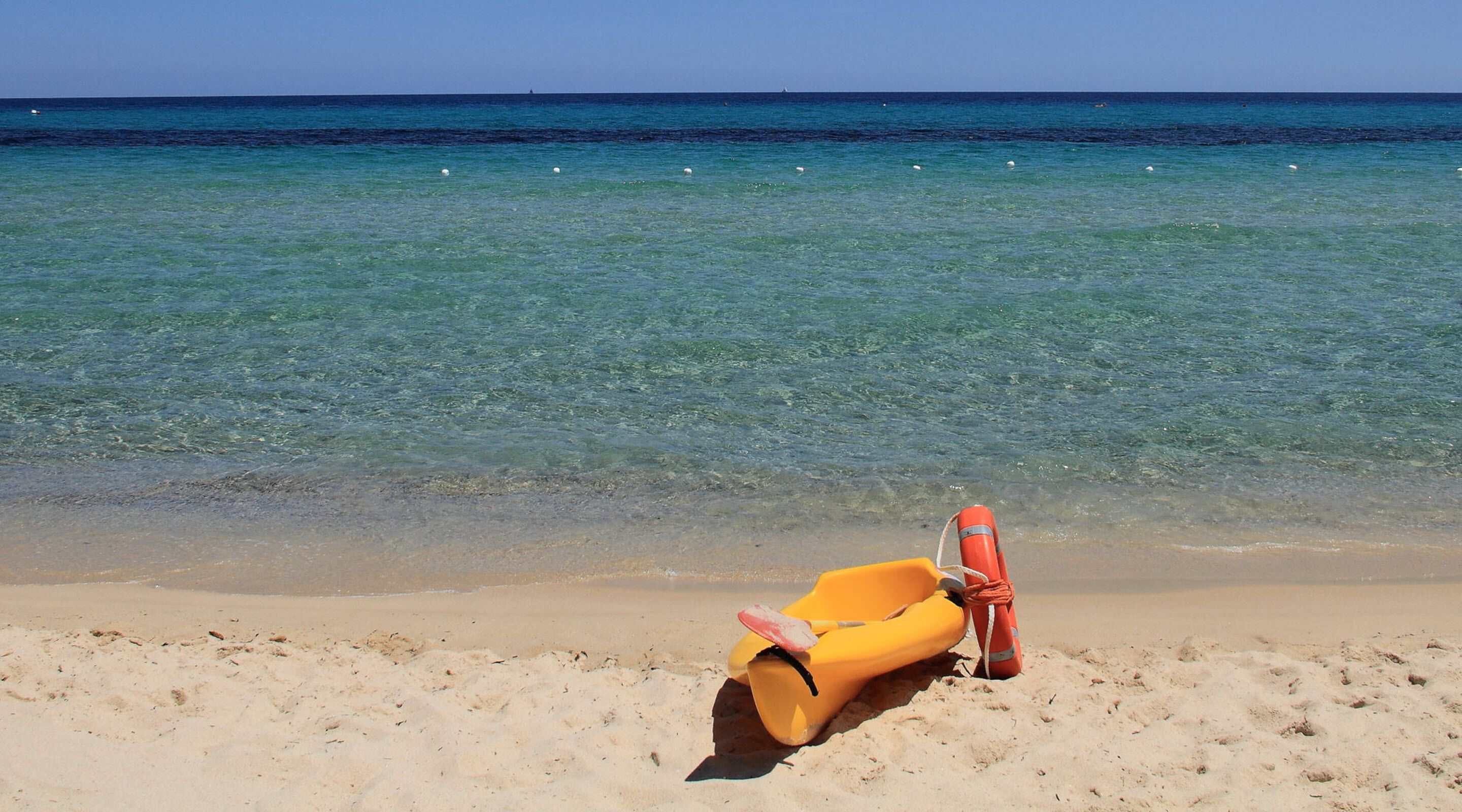 Una playa con agua cristalina, una silla de playa amarilla y un flotador salvavidas rojo.