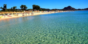 Una playa con agua cristalina, sombrillas y gente.