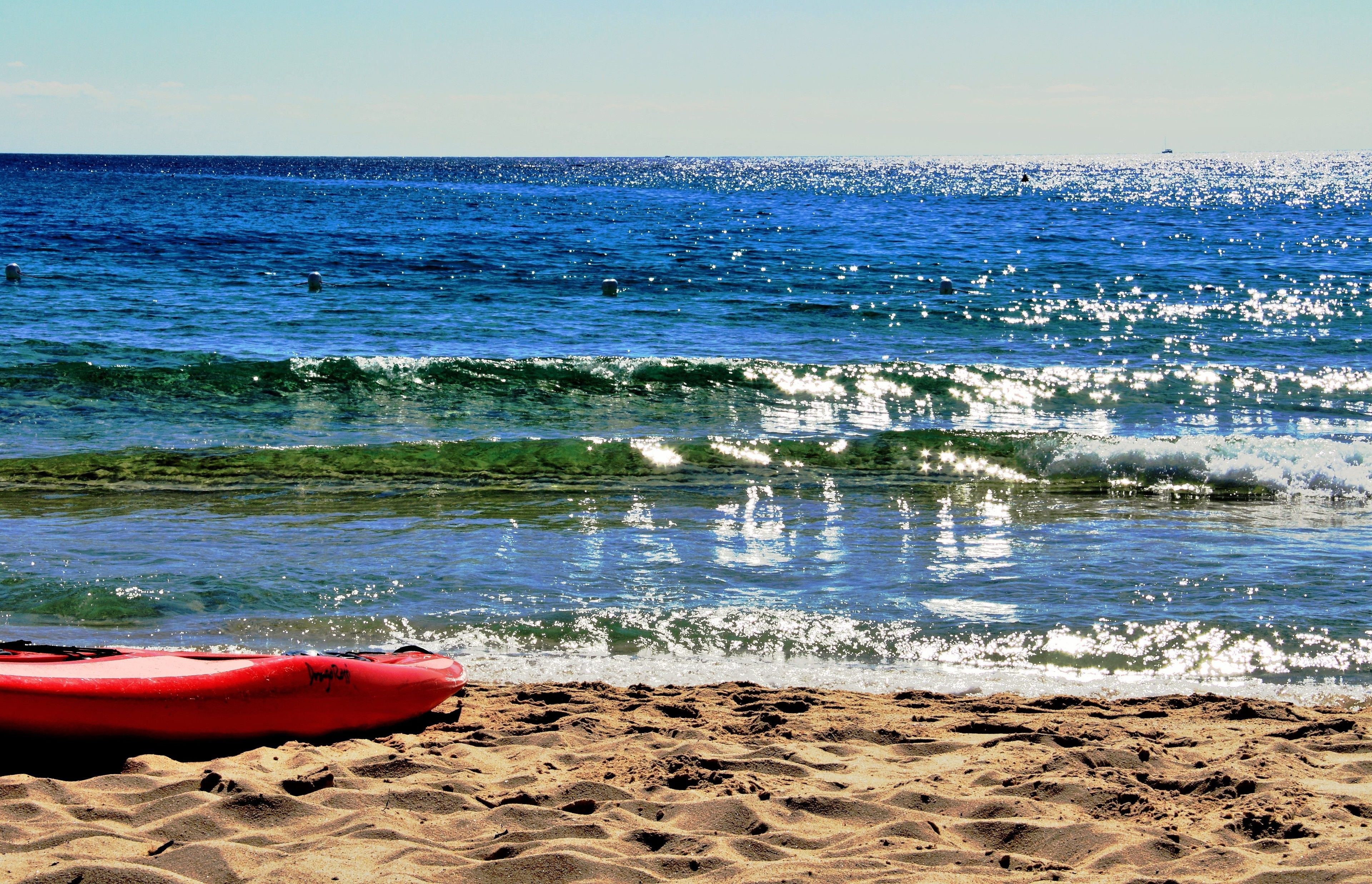 A beach with a red kayak and footprints in the sand.