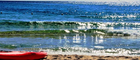 A beach with a red kayak and footprints in the sand.