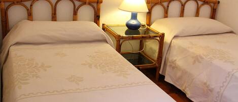 Two single beds with wooden headboards, a nightstand with a lamp, and a floral-patterned bedspread.
