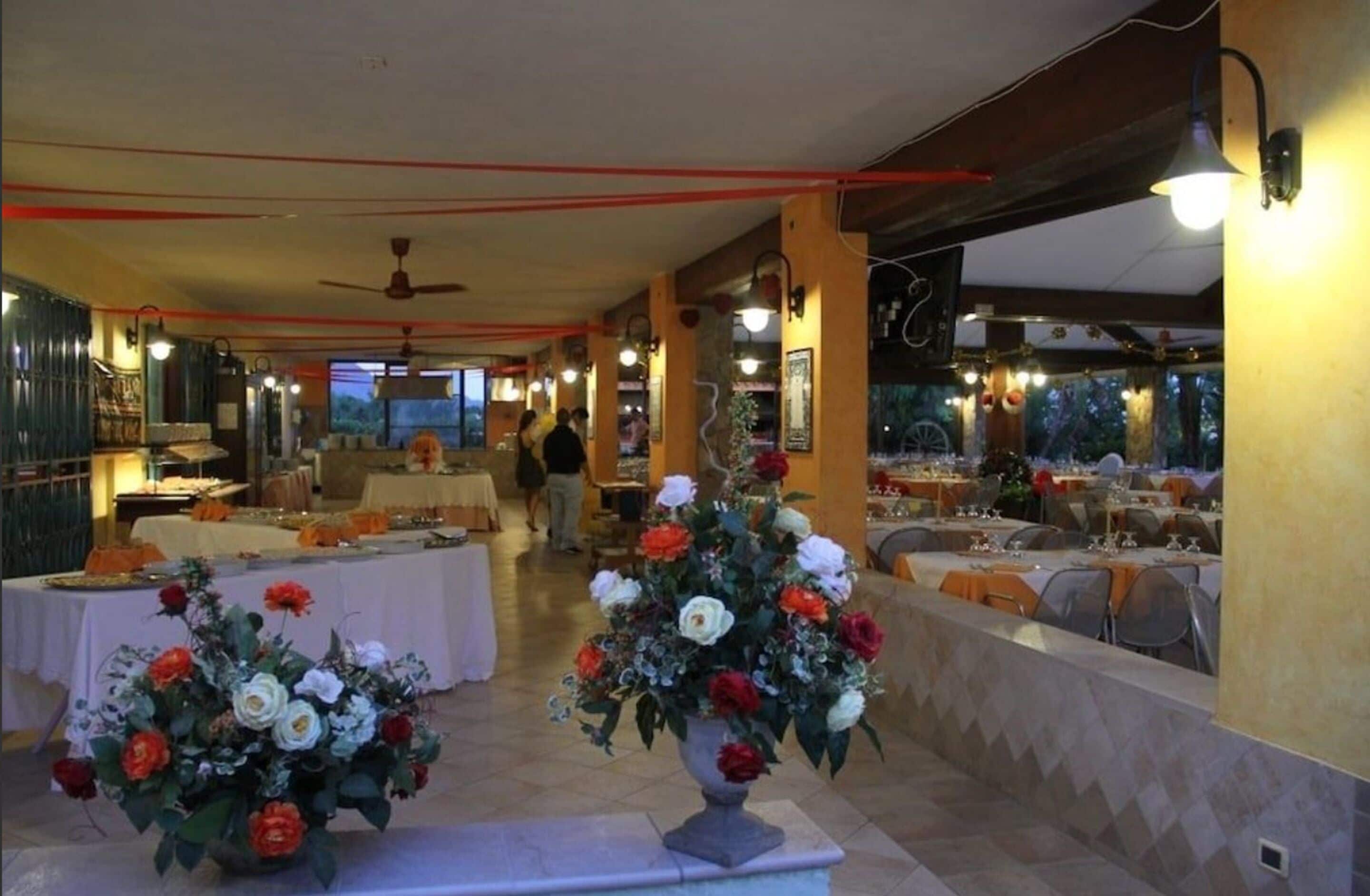 Un restaurant où les tables sont dressées pour le service, décorées de compositions florales et offrant une vue sur l’extérieur.