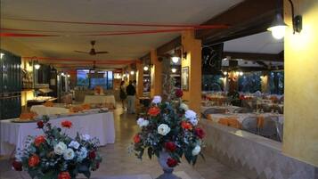 Un ristorante con tavoli apparecchiati per la cena, decorato con composizioni floreali e vista sull'esterno.