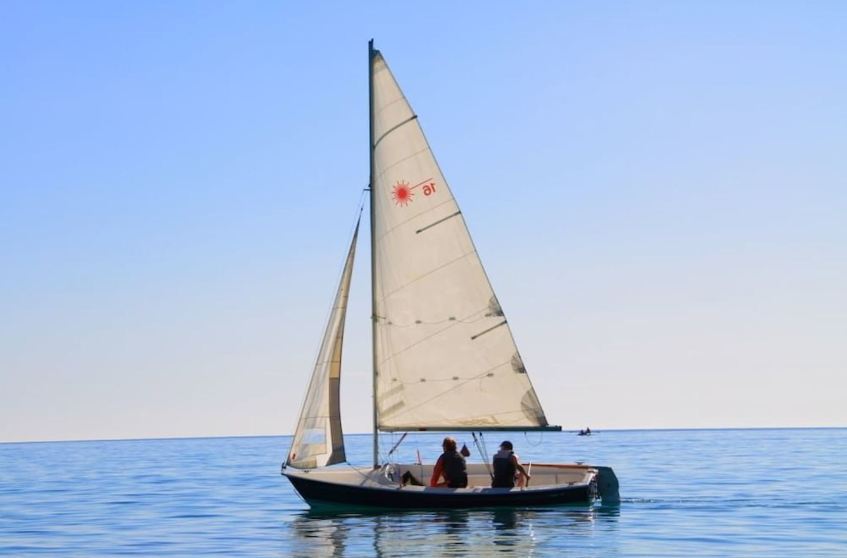 A sailboat with two people on board, sailing on calm water.