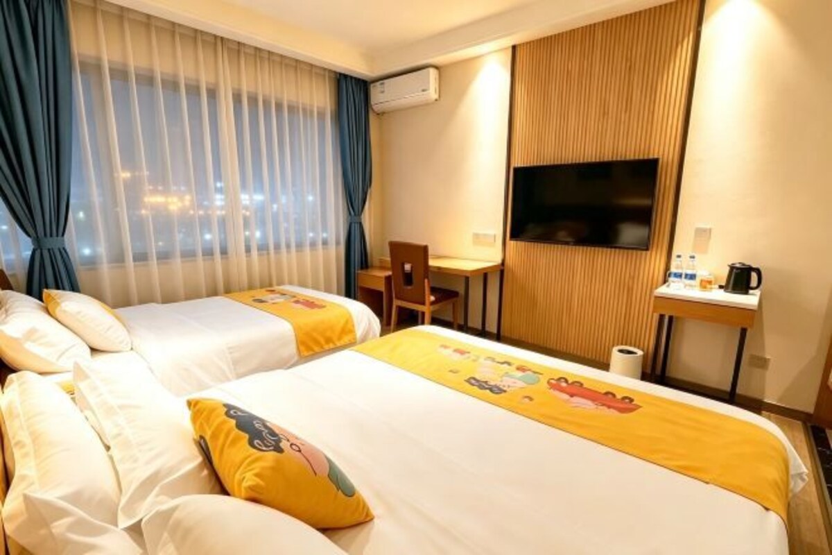 Une chambre d’hôtel avec deux lits, un bureau, une chaise, une télévision et une fenêtre avec des rideaux.