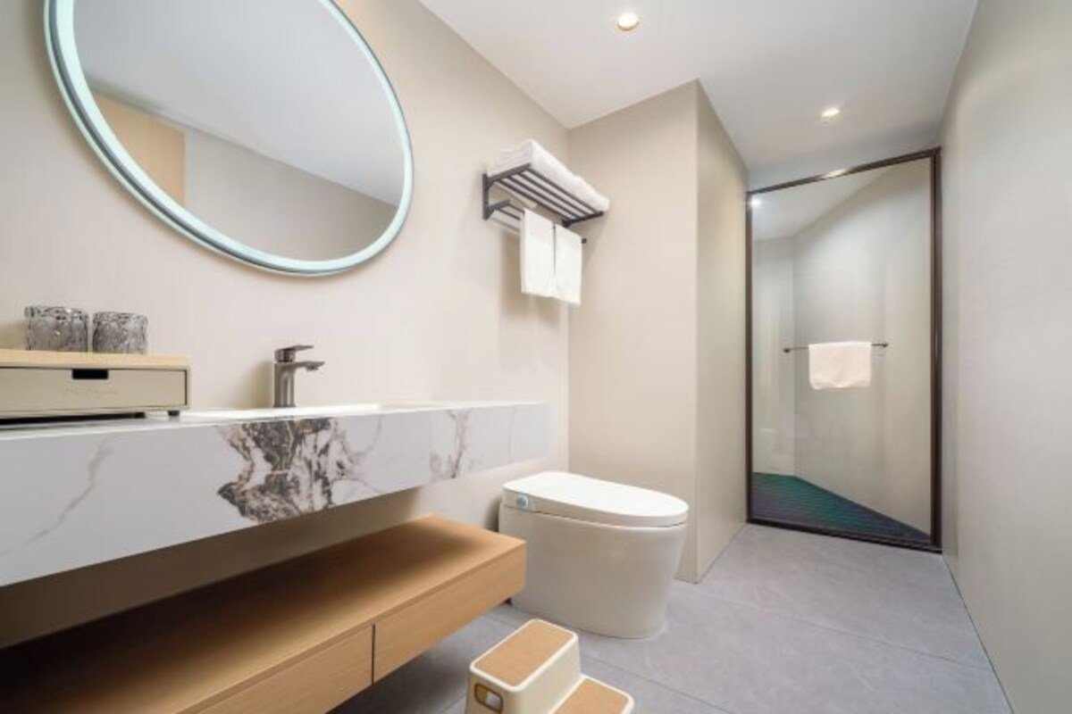 Une salle de bain moderne avec un meuble-lavabo en marbre, un miroir rond, une cabine de douche en verre et des toilettes.